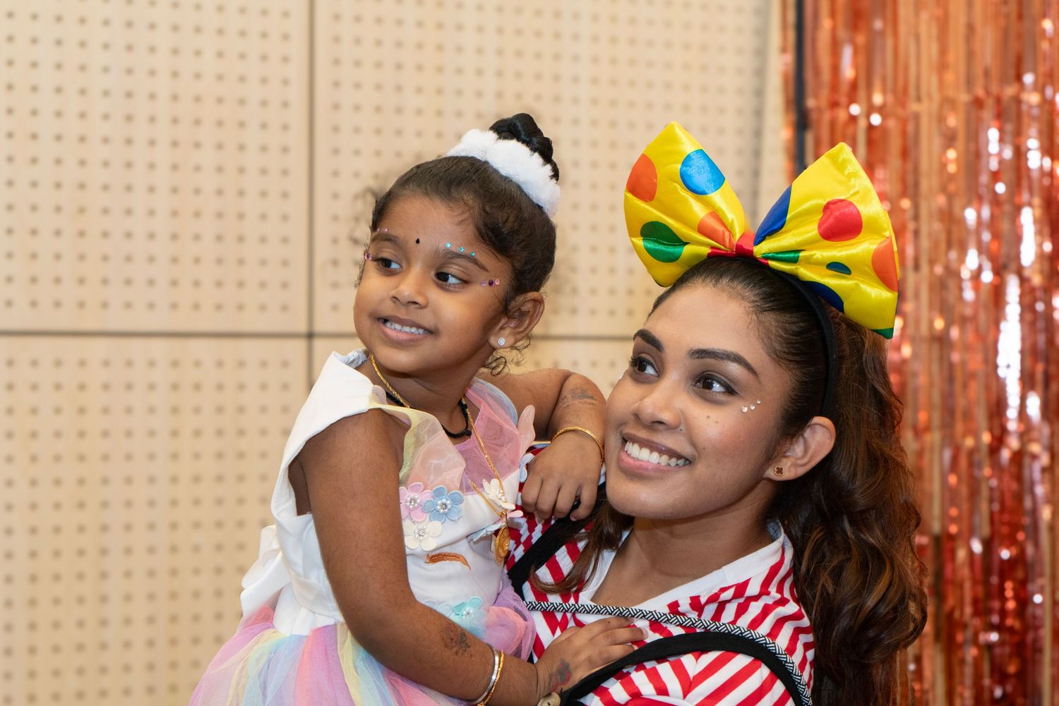 A festive gathering shows people celebrating with colorful decorations and party attire.