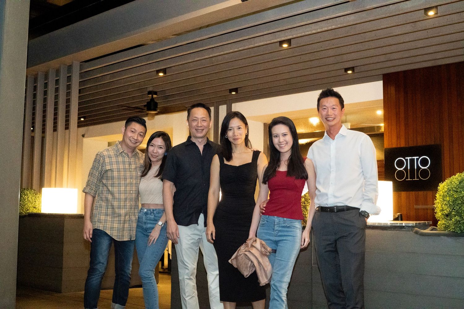 Group of six friends smiling together outside Otto restaurant at night.
