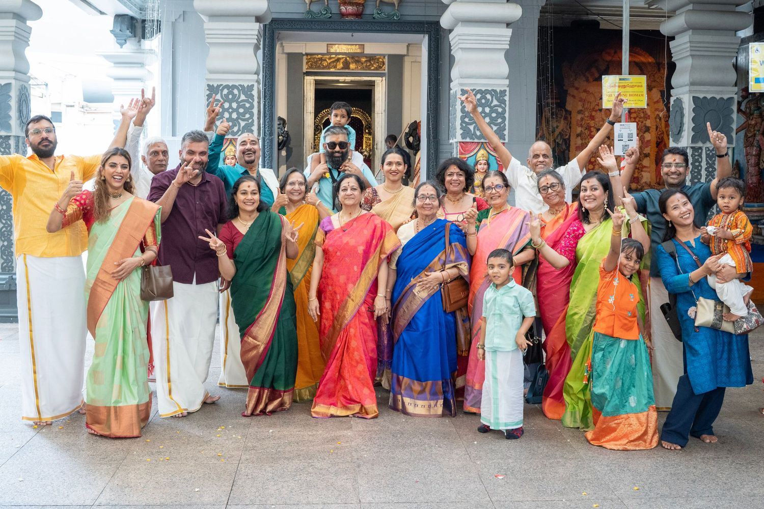 Colorful group photo outside temple entrance with people wearing traditional Indian saris.