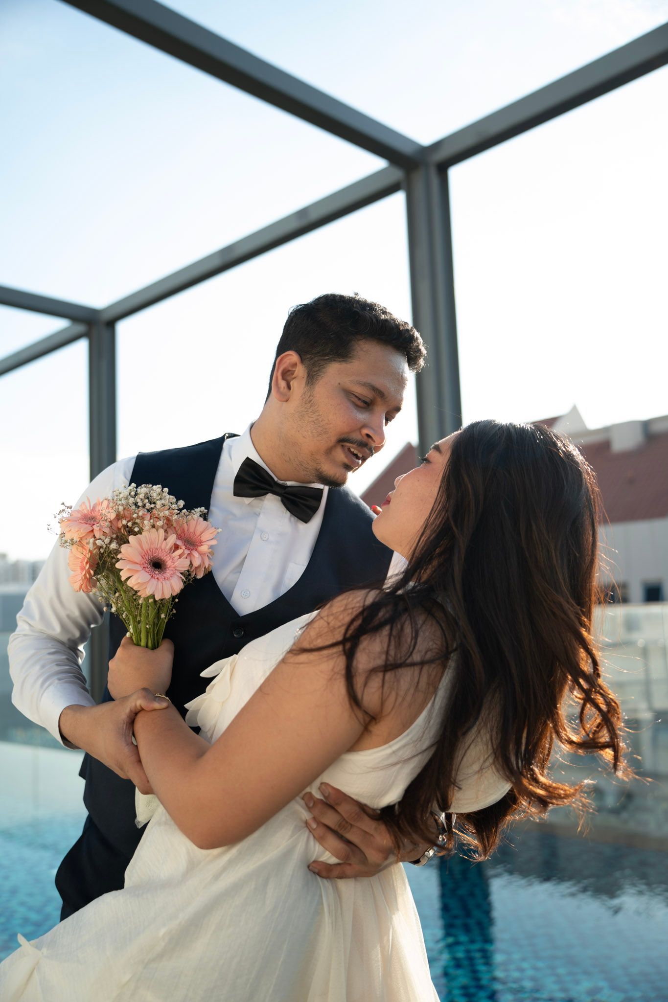 Romantic wedding couple sharing intimate moments by a pool during sunset photoshoot.