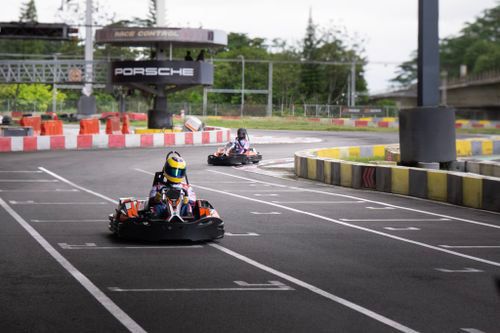 Go-karts racing on an outdoor track with safety barriers and clear lane markings.