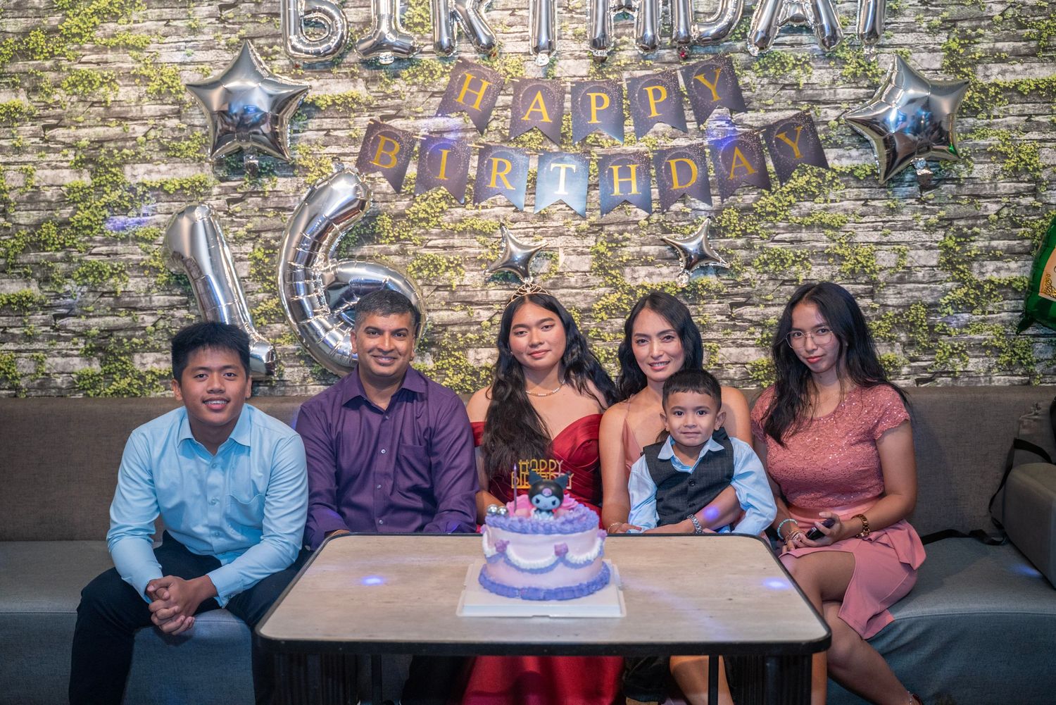 Birthday celebration with cake and guests gathered around a rustic stone wall backdrop.