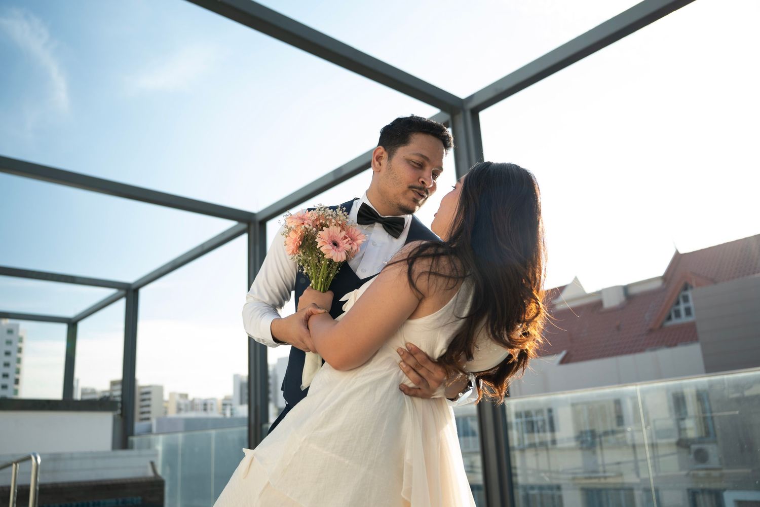 Romantic rooftop moment between couple in wedding attire against city skyline.
