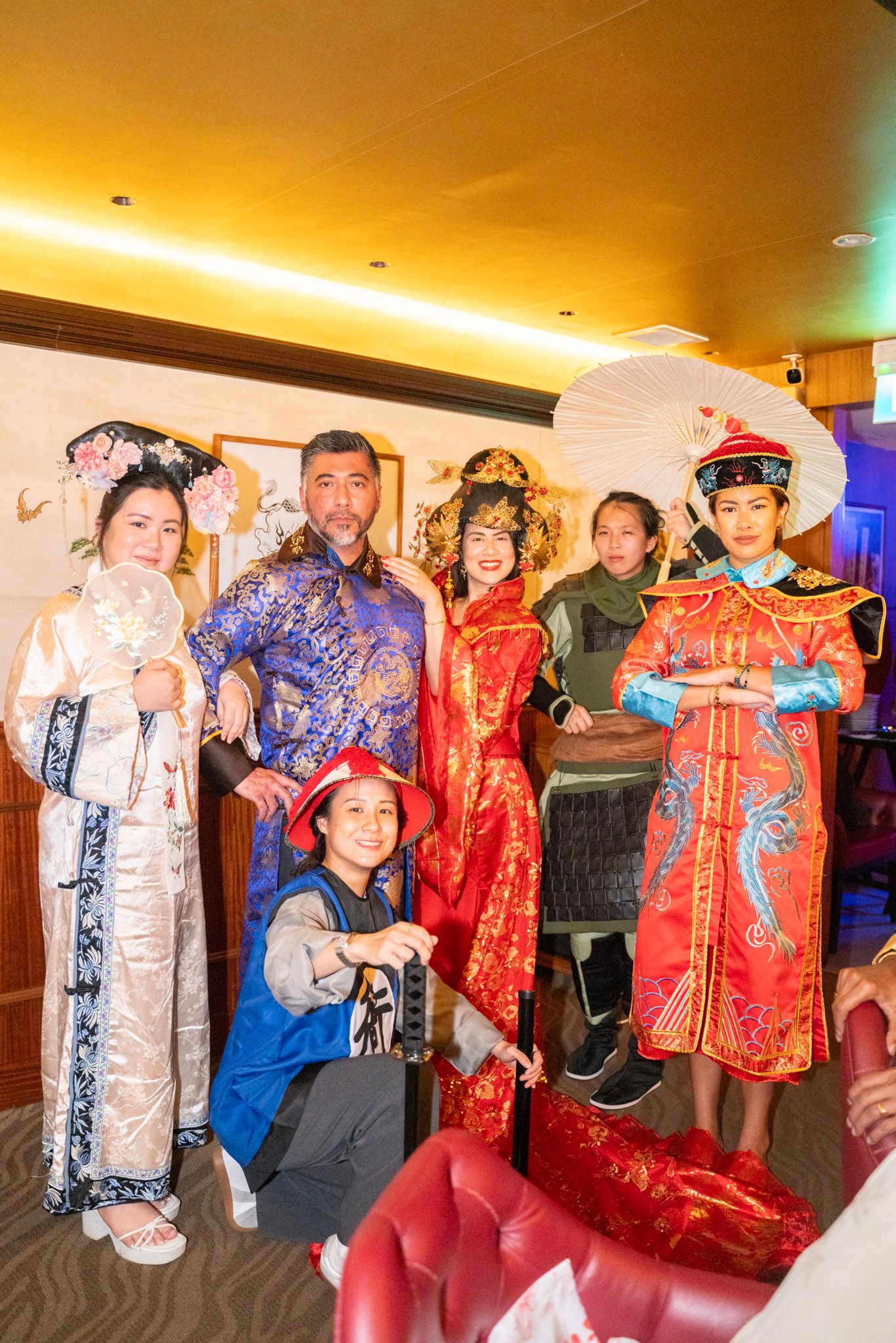 People wearing traditional Chinese robes and costumes posing together in a warmly lit room.
