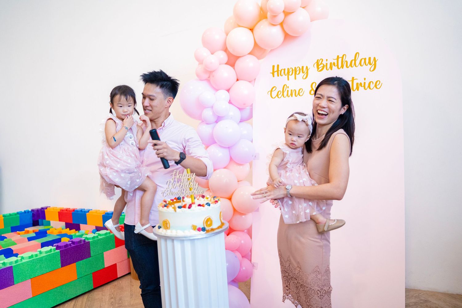 Family celebrating a birthday party with balloons, cake, and a Happy Birthday banner in a decorated venue.