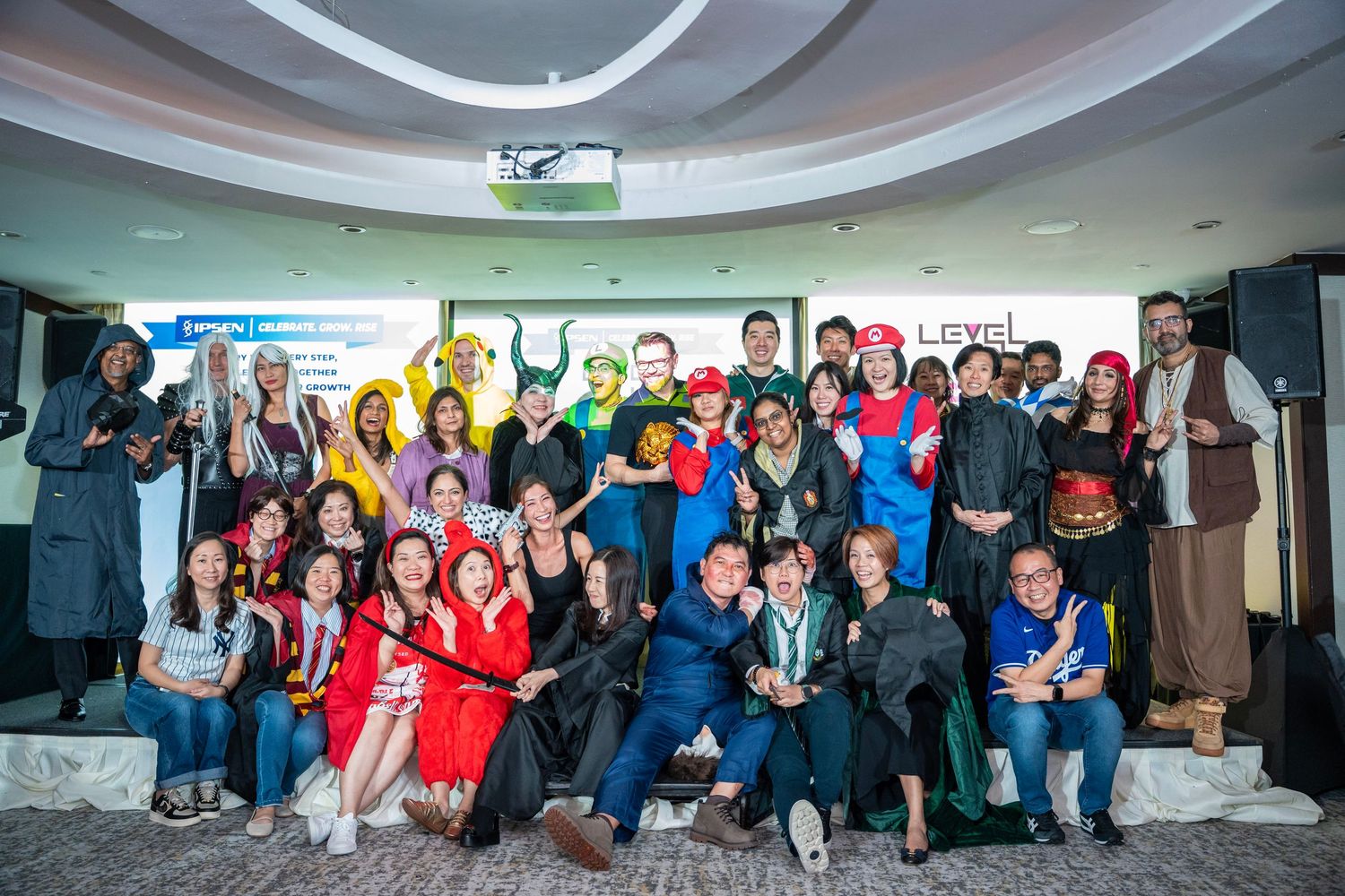 Large group photo of event attendees gathered under curved ceiling with modern lighting.