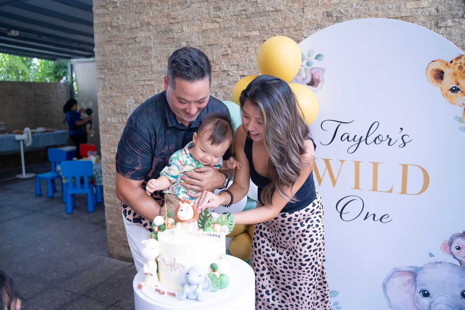 Parents celebrate baby Taylor's Wild One first birthday party with cake cutting ceremony at safari themed event.