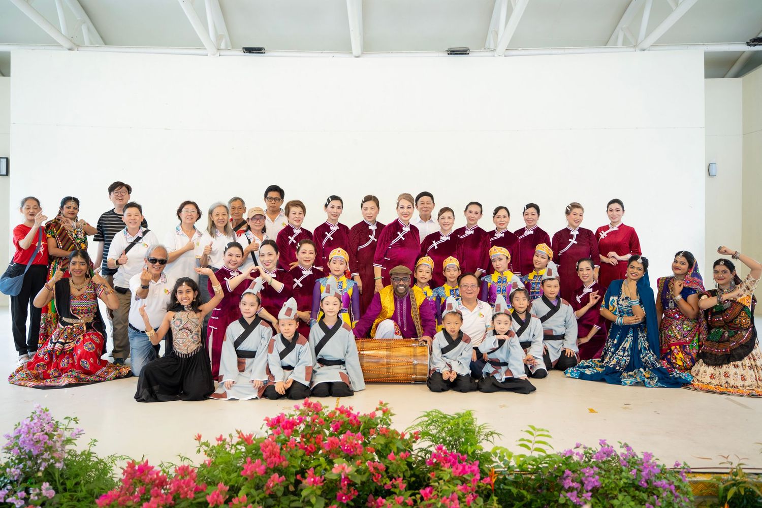 Large group photo of people wearing colorful traditional attire gathered outdoors for a cultural celebration.