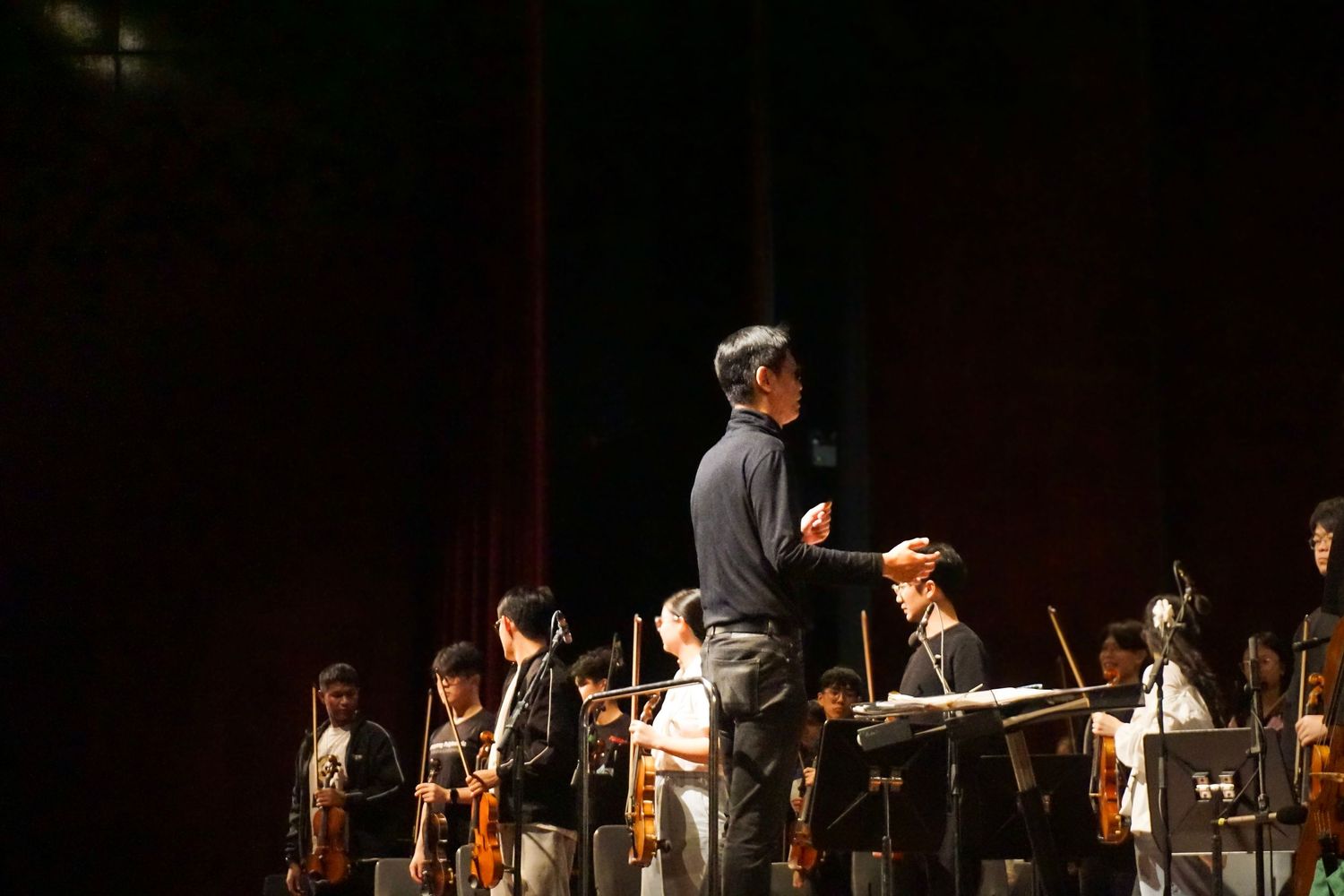 Orchestra performers on stage during a classical music concert with dramatic lighting.