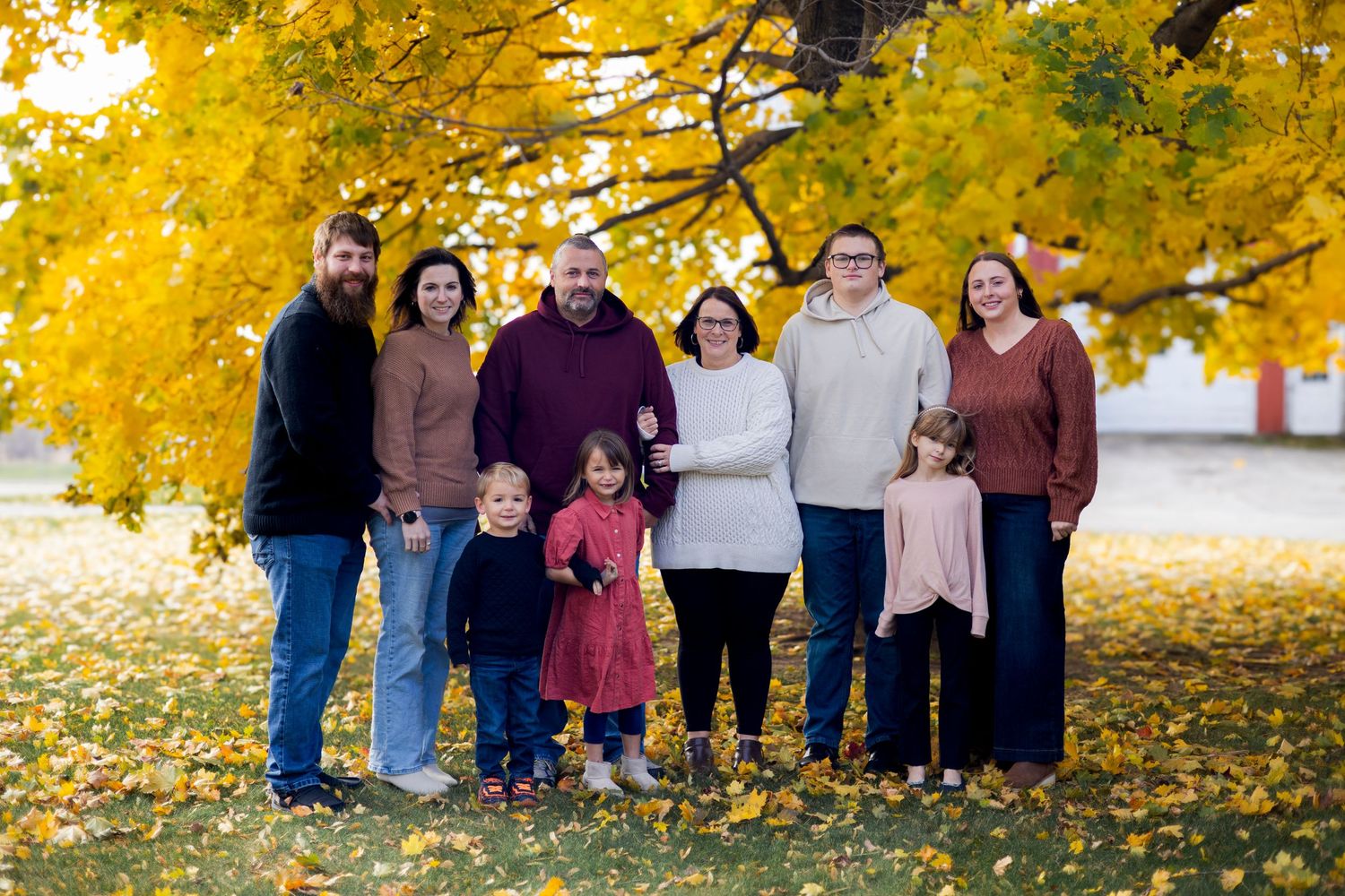 A group stands together under vibrant yellow autumn trees with fallen leaves scattered on the ground.