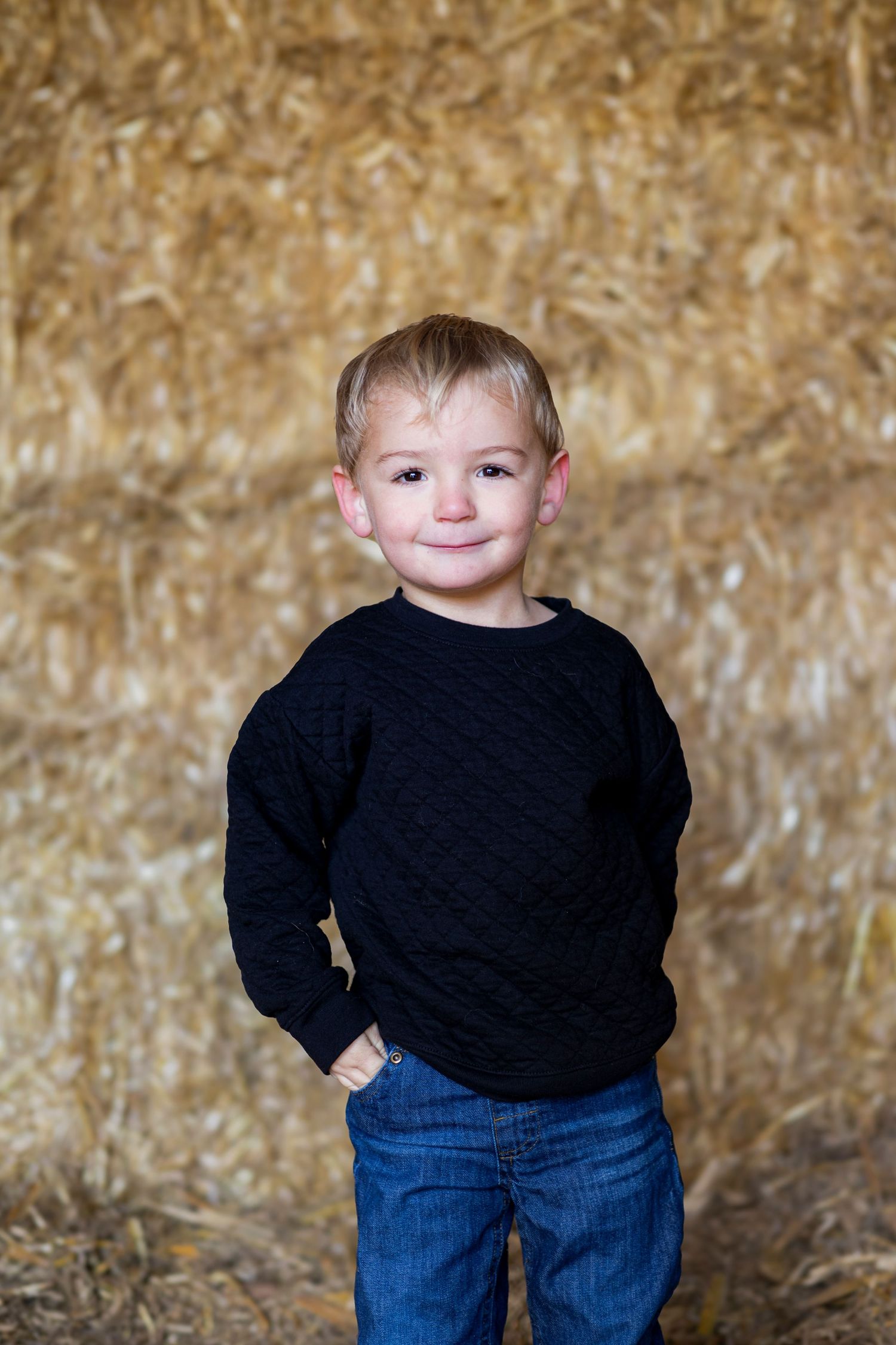 A small child wearing a black sweater and blue jeans poses playfully against a textured gold-colored backdrop.