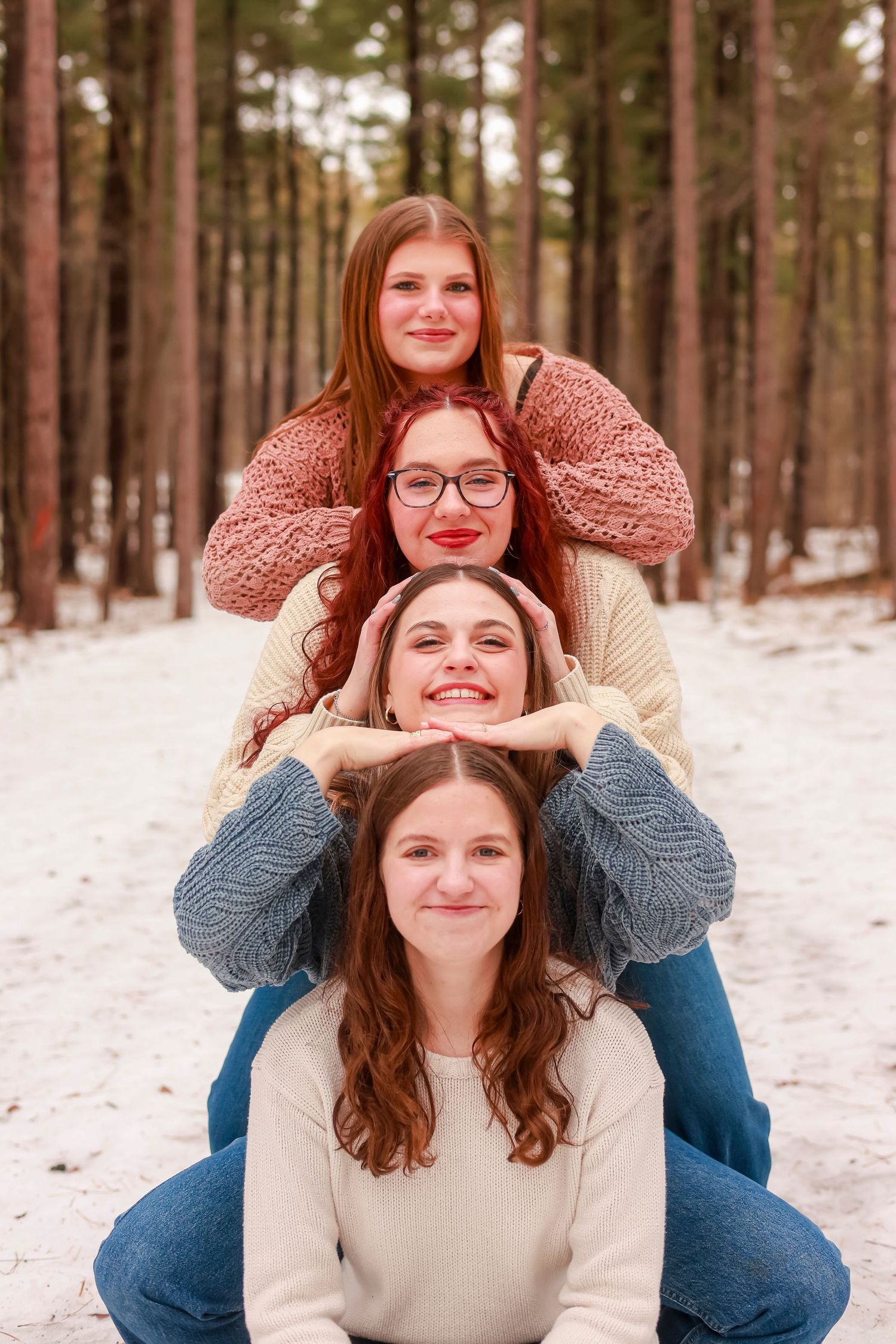 Four people in cozy winter sweaters pose together in a snowy forest setting.