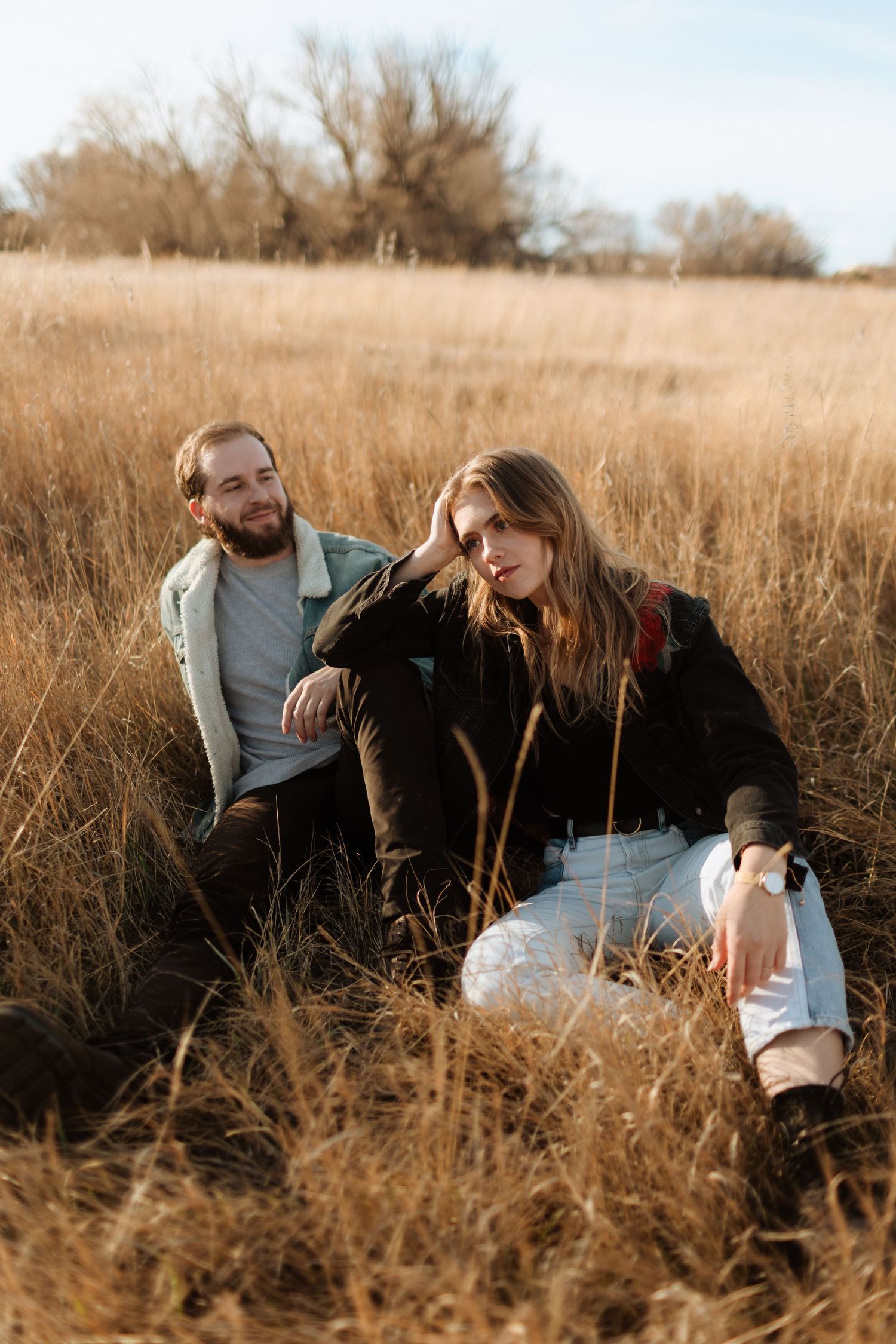 A couple relaxes together in a golden field of tall grass during autumn.