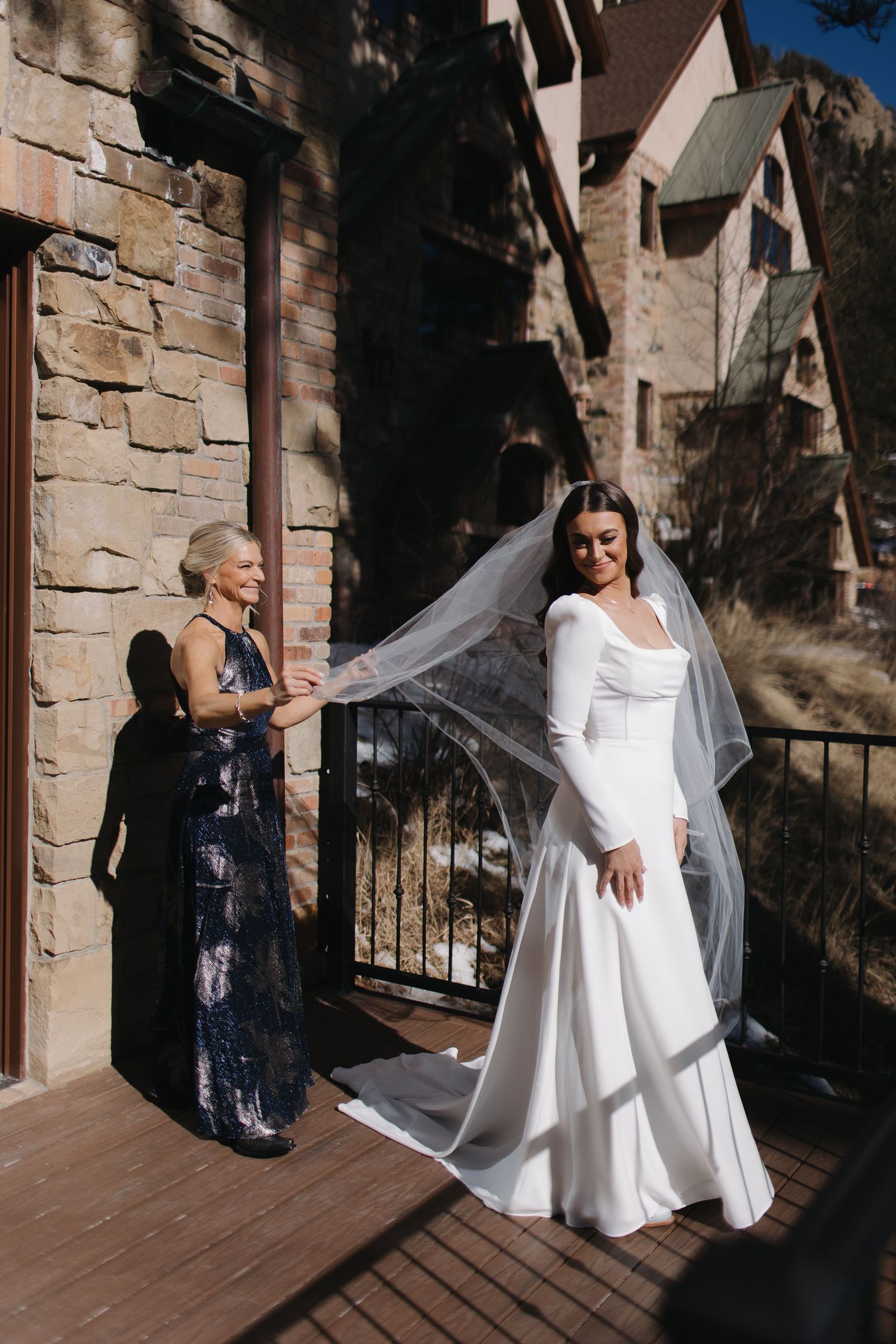 A flowing white wedding gown with long train being arranged on a stone balcony.