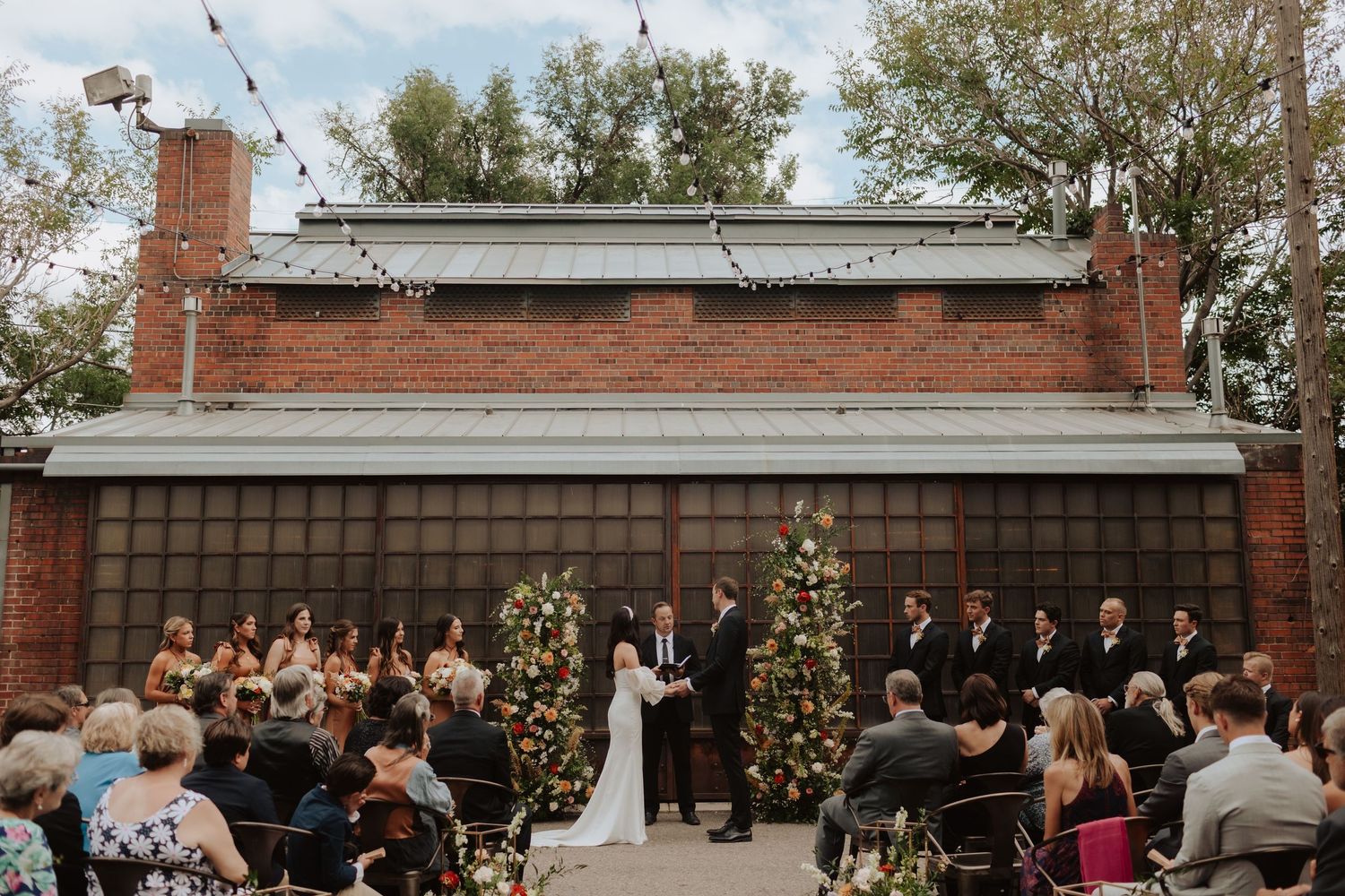 Outdoor wedding ceremony setup with brick wall backdrop and floral decorations.