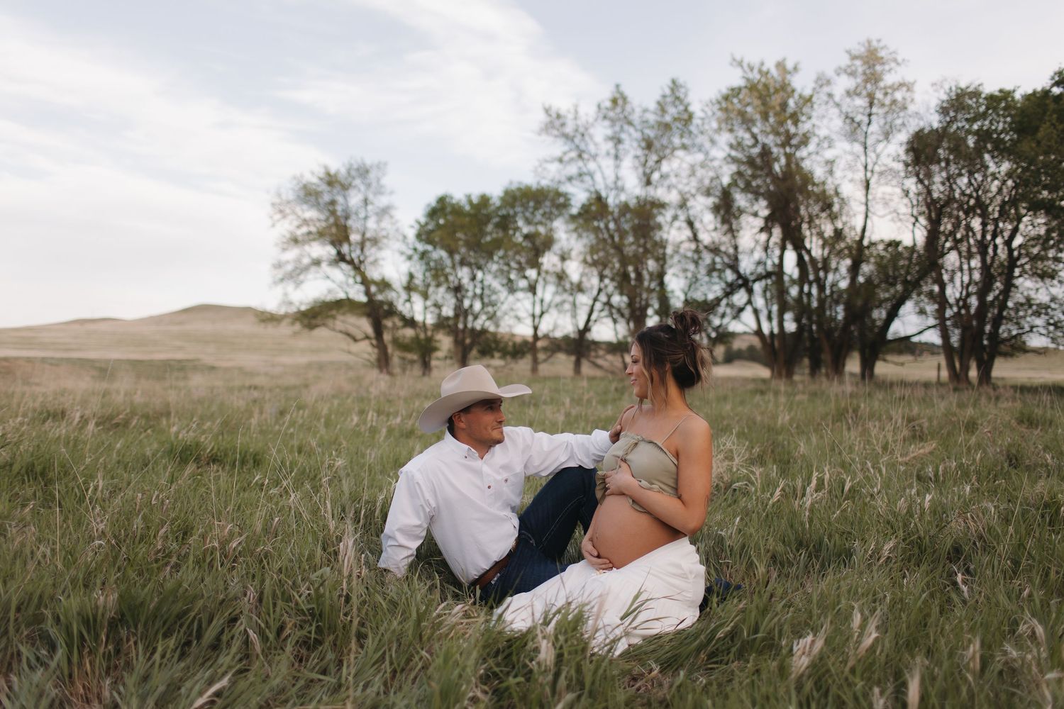 Intimate family photoshoot in a serene grassland setting with scattered trees.