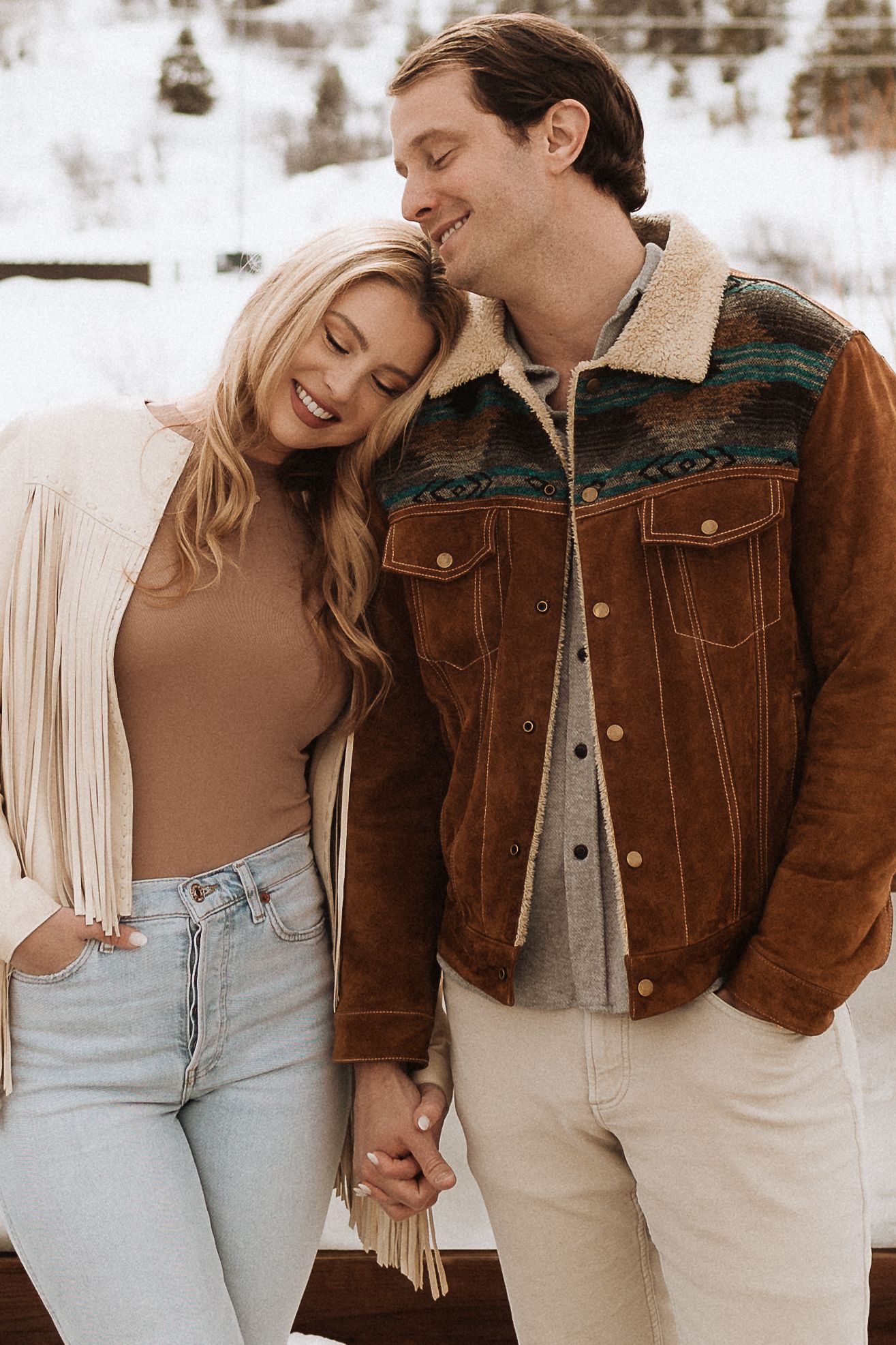 Stylish couple in western wear sharing tender moments against snowy backdrop.