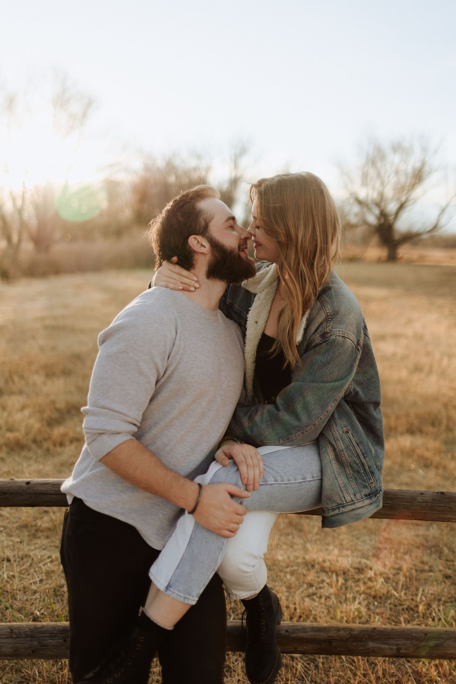 A couple shares an intimate moment while sitting on a wooden fence in golden afternoon light.