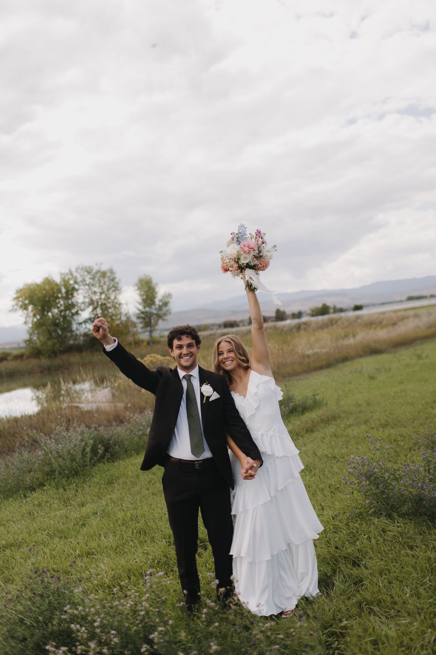 Newlyweds celebrate with raised arms in a scenic mountain landscape.
