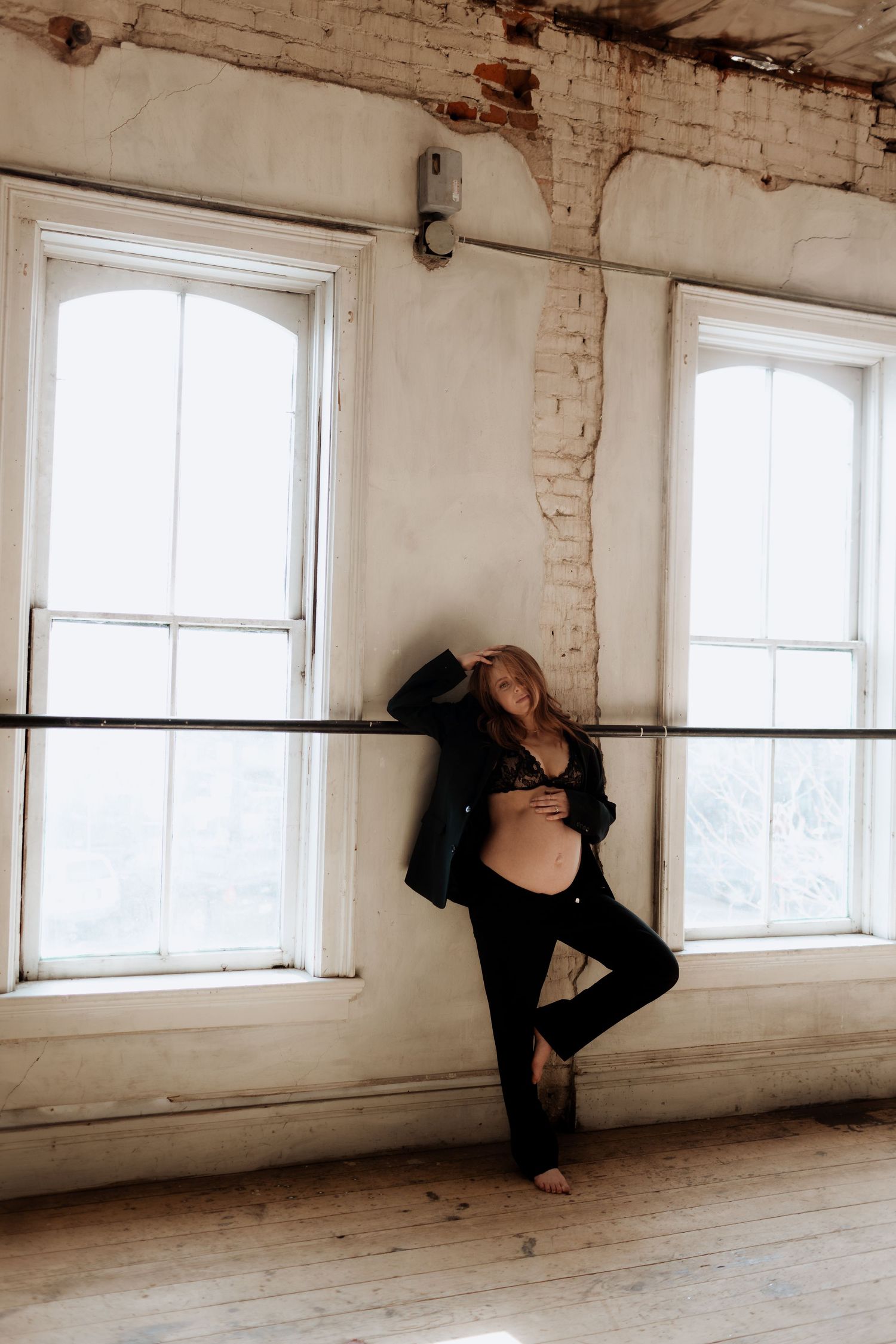 A maternity photo in an industrial loft space with exposed brick and large windows.