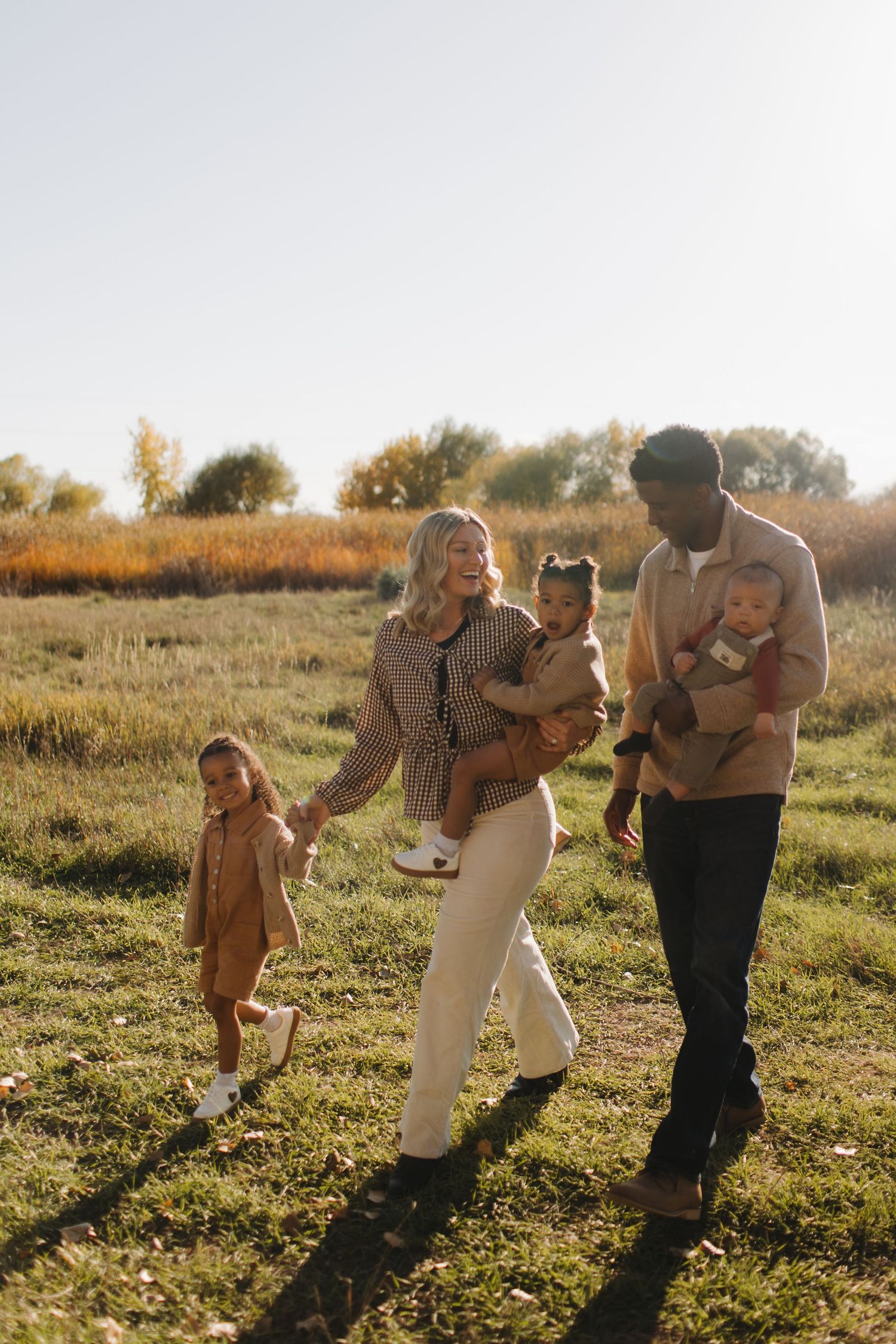 A family walks together through a golden autumn field at sunset.