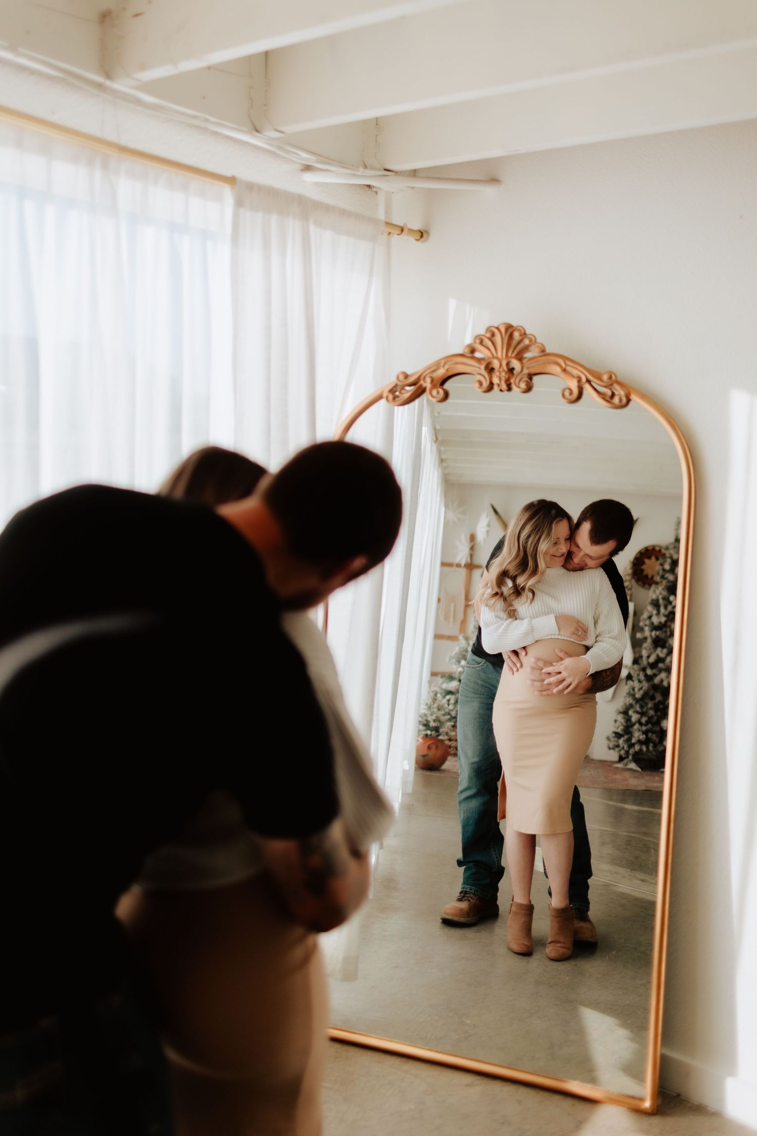 Indoor photo session with ornate gold mirror and white curtained windows.