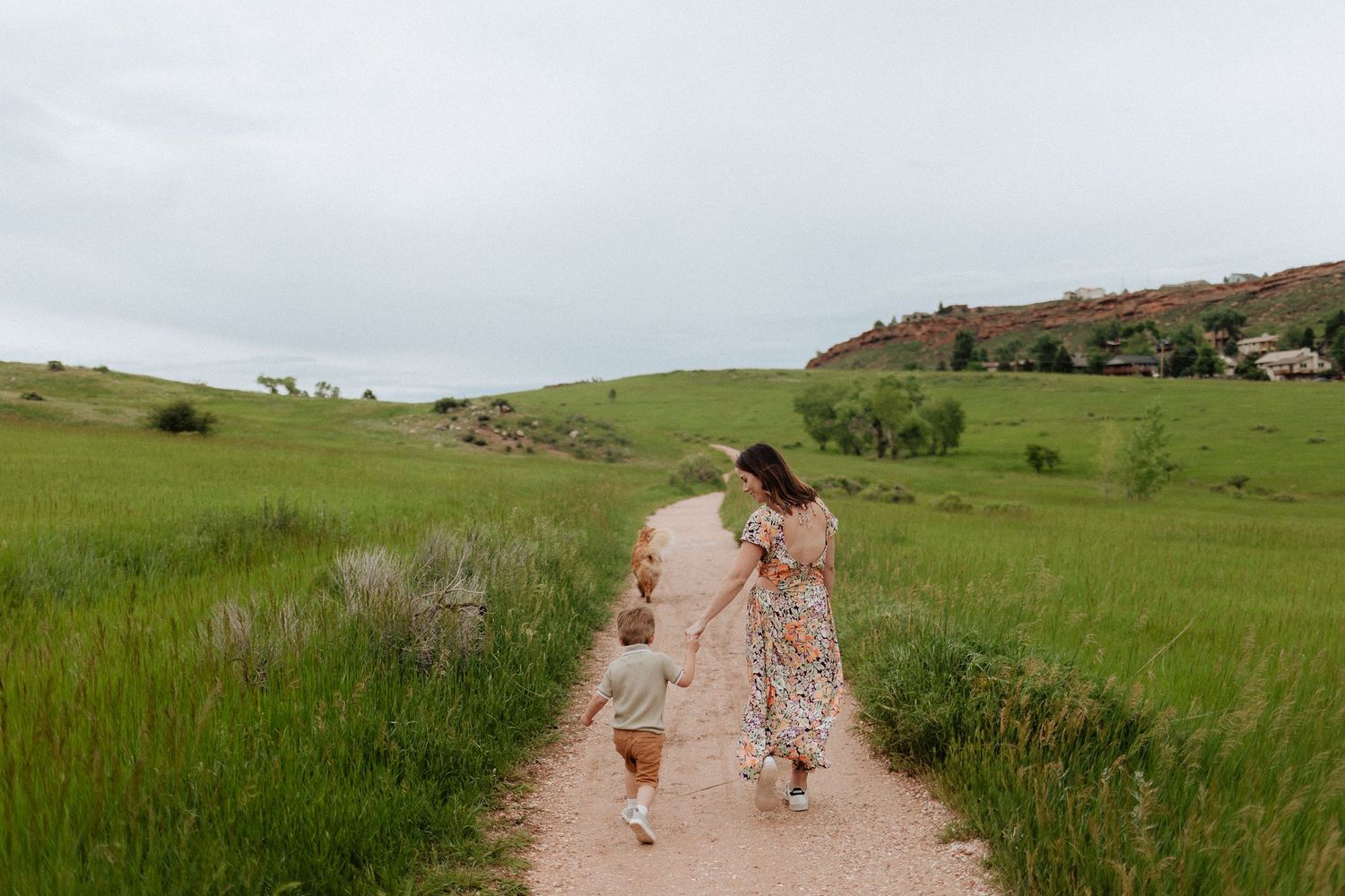 Couple runs playfully down dirt path through green rolling hills.