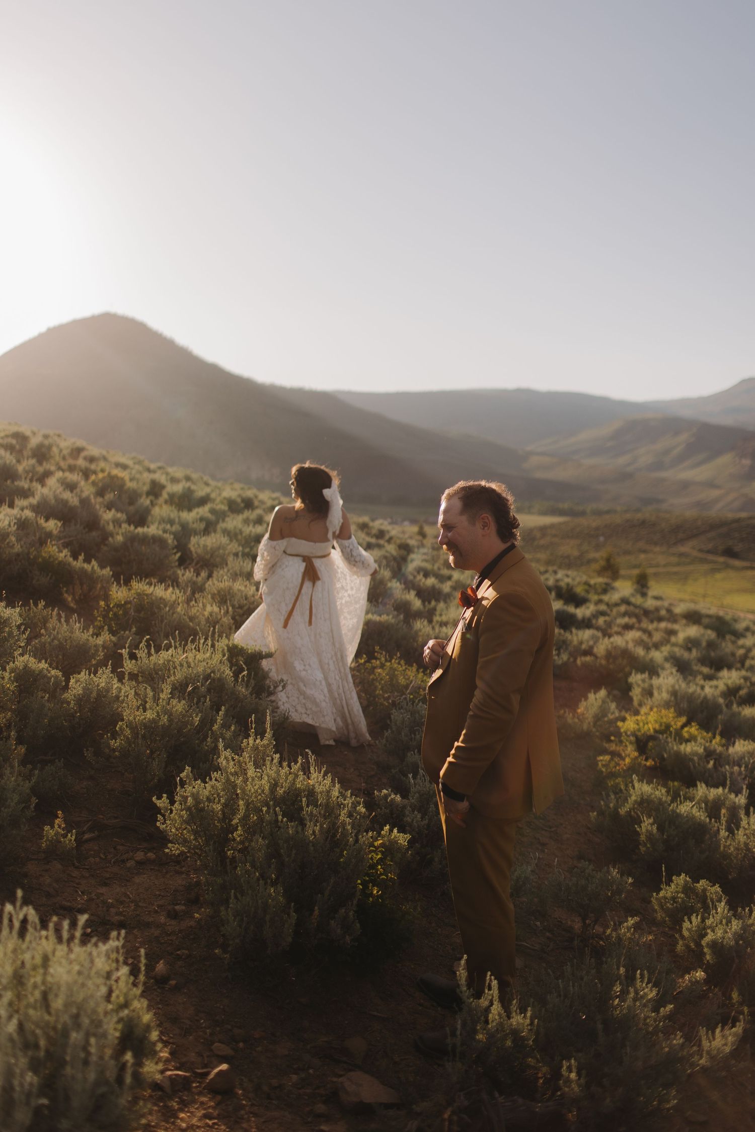 A couple stands together in a desert landscape with sagebrush and rolling hills at golden hour.