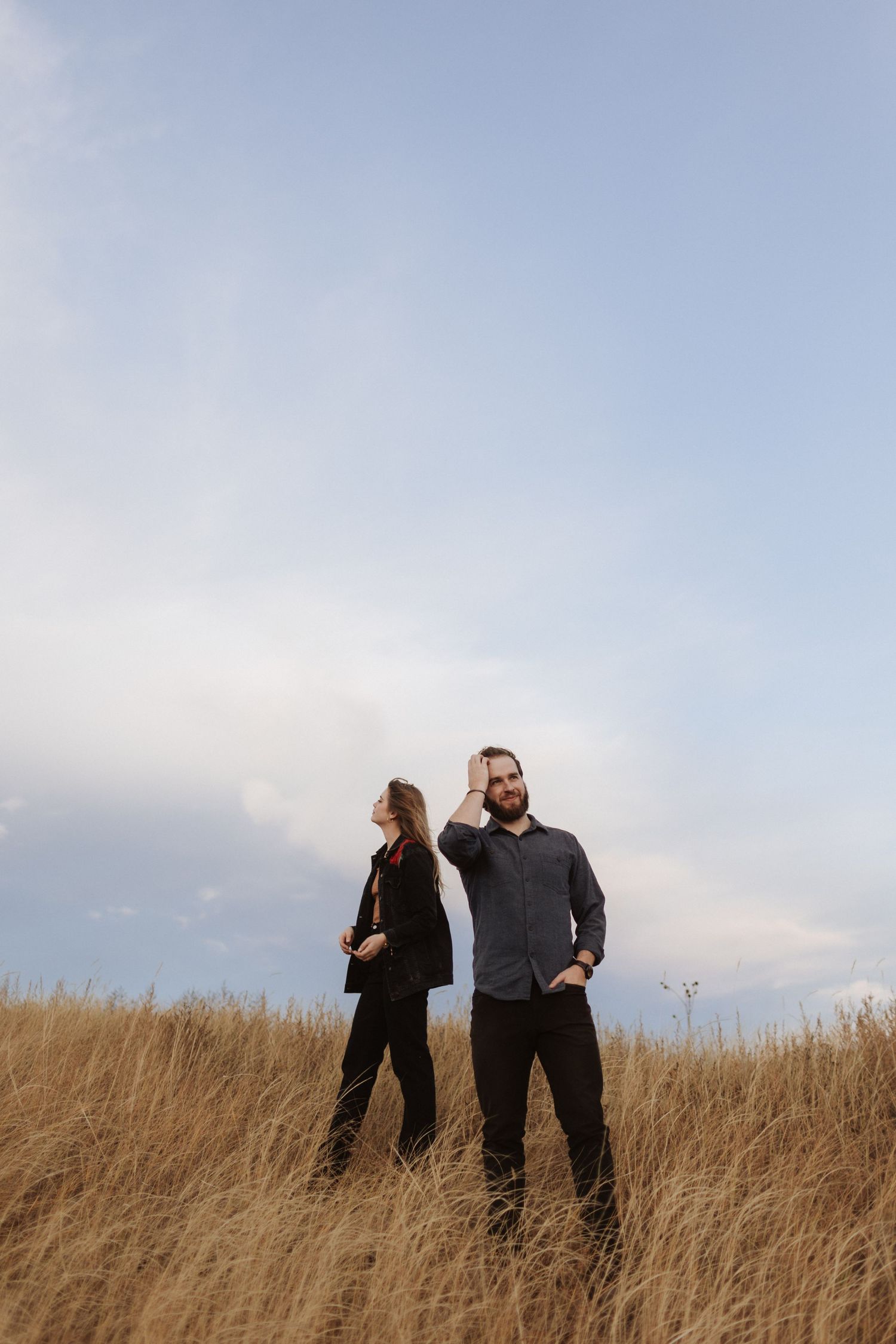 A couple walks through tall prairie grass against a bright blue sky.