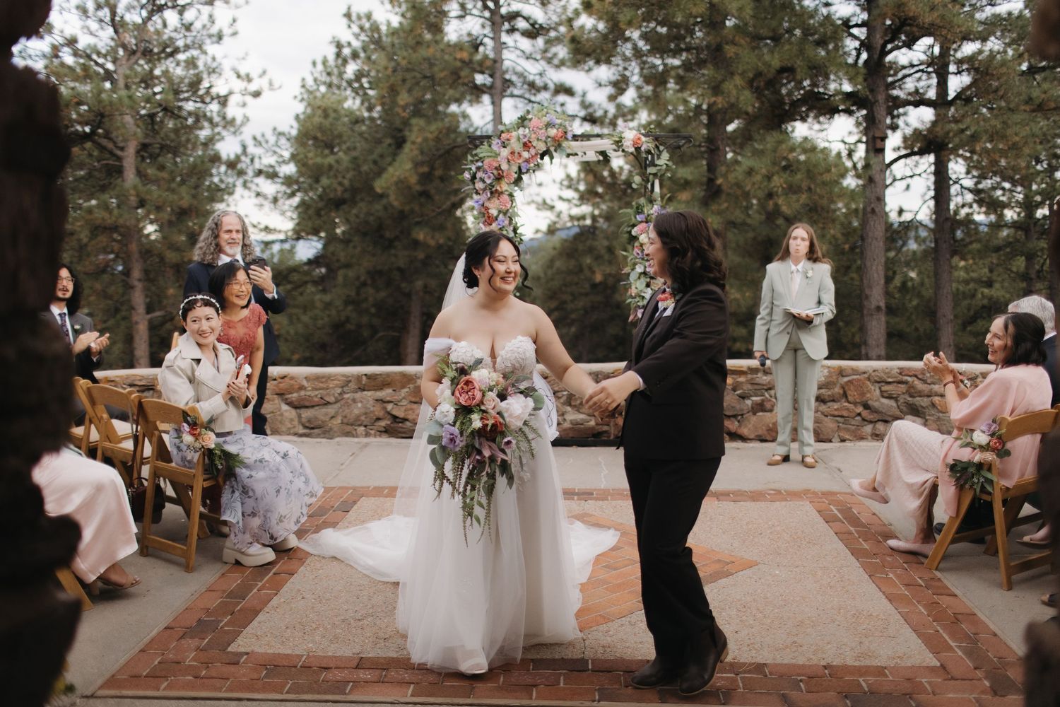 Wedding ceremony in outdoor mountain setting with guests seated on rustic benches.