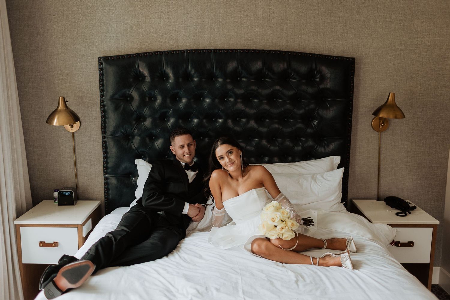 Wedding couple relaxing on hotel bed with elegant decor and lighting.