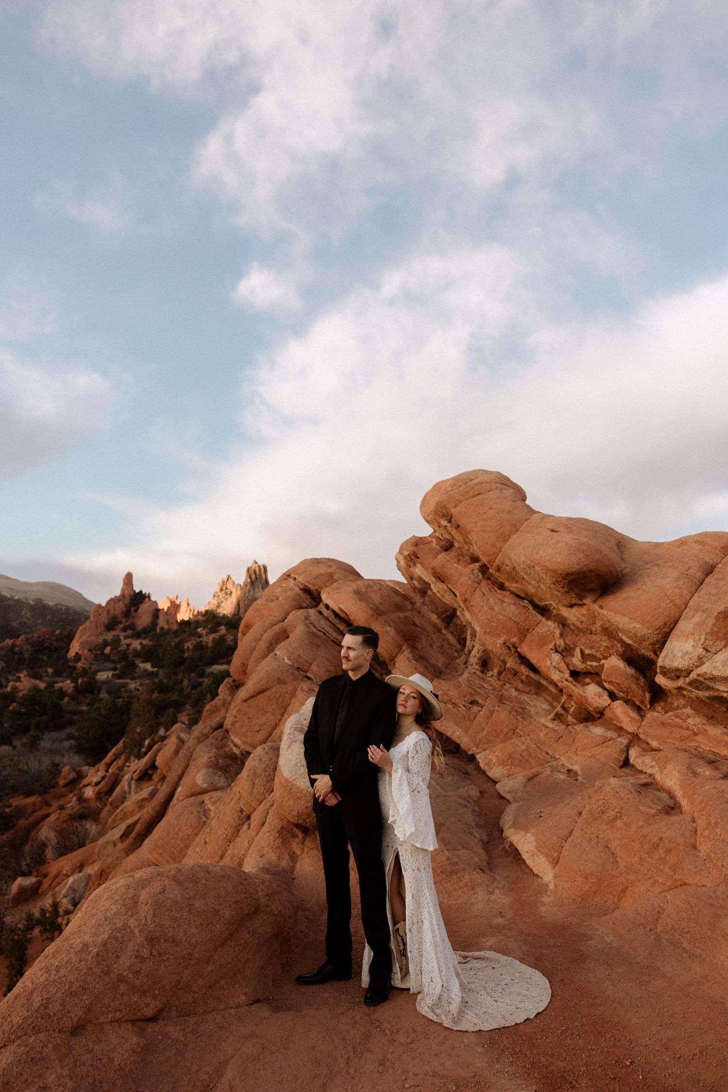 Couple in wedding attire posing among dramatic desert rock formations at sunset.