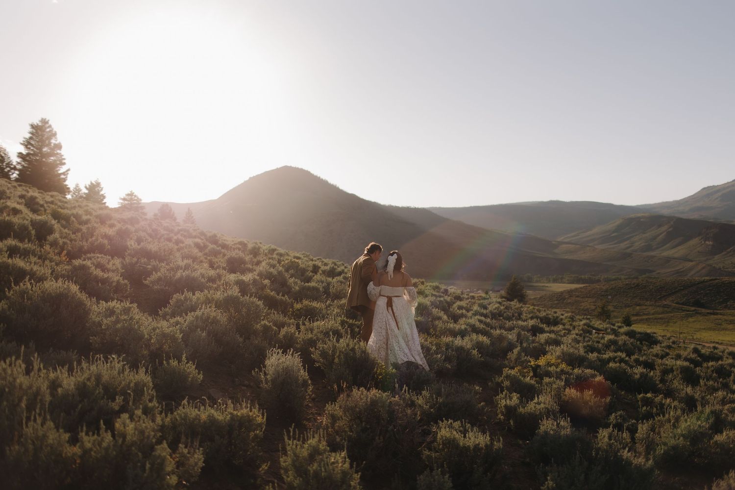 Scenic mountain landscape at sunset with golden light filtering through trees and rolling hills.
