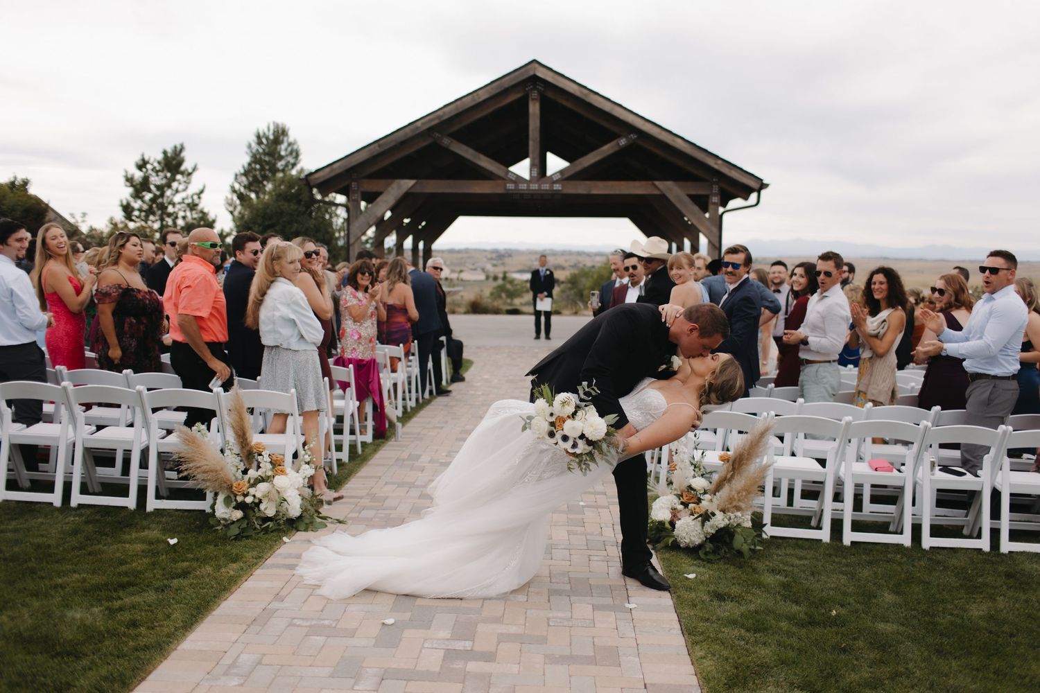 Outdoor wedding venue with white chairs set up on grass facing wooden pavilion structure.