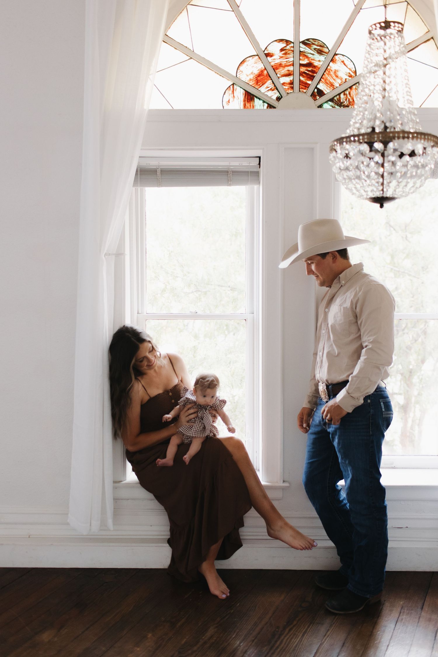 A family shares a tender moment by a bright window with elegant crystal chandeliers in an elegant white room.