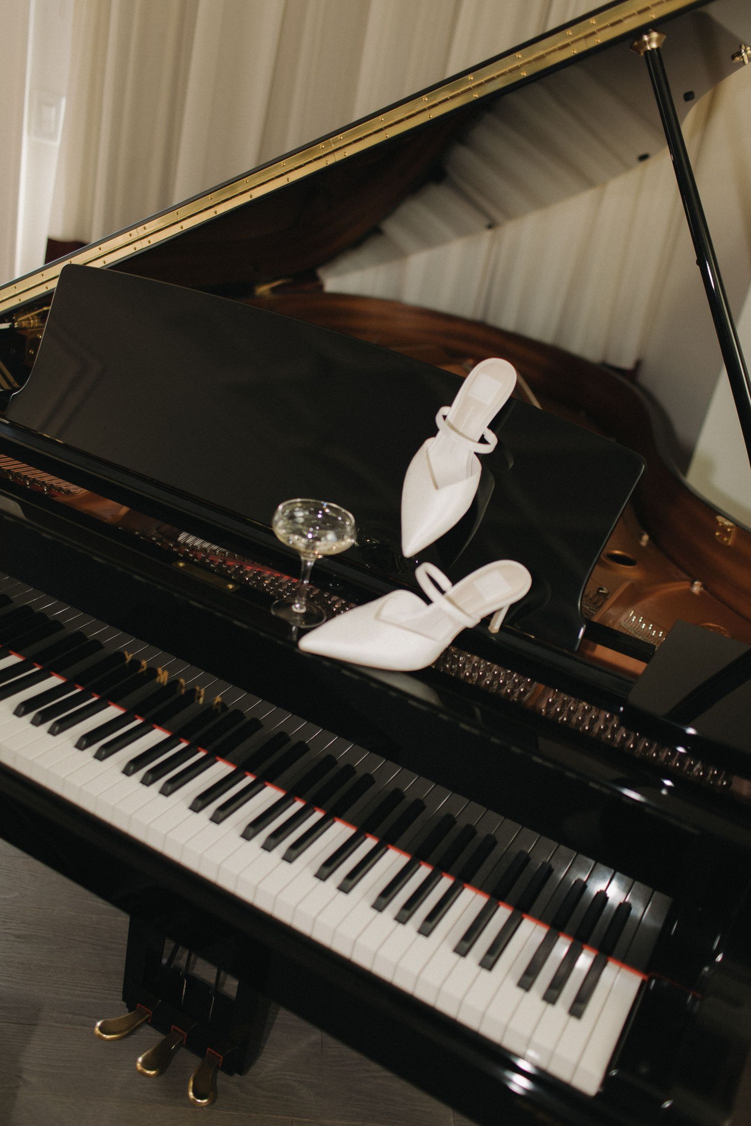 White bridal shoe placed on black grand piano keys in artistic wedding detail shot.