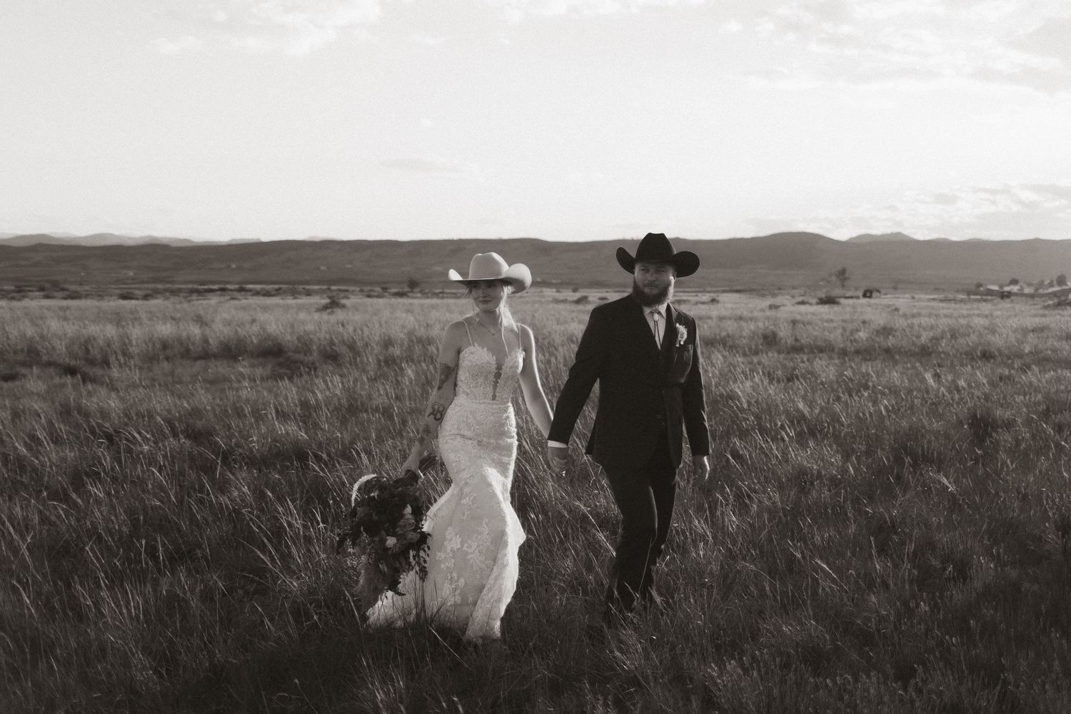 Silhouetted couple walking through golden grass field with mountains in background.