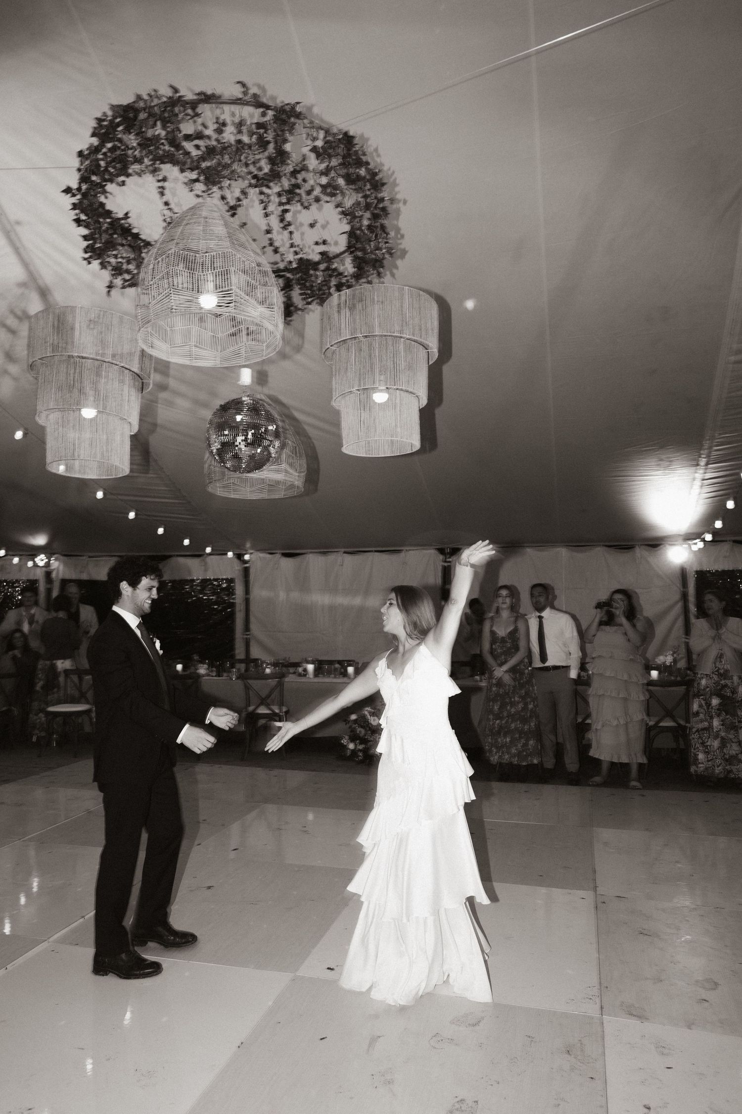 A couple dances under elegant chandeliers and floral decorations at their wedding reception.