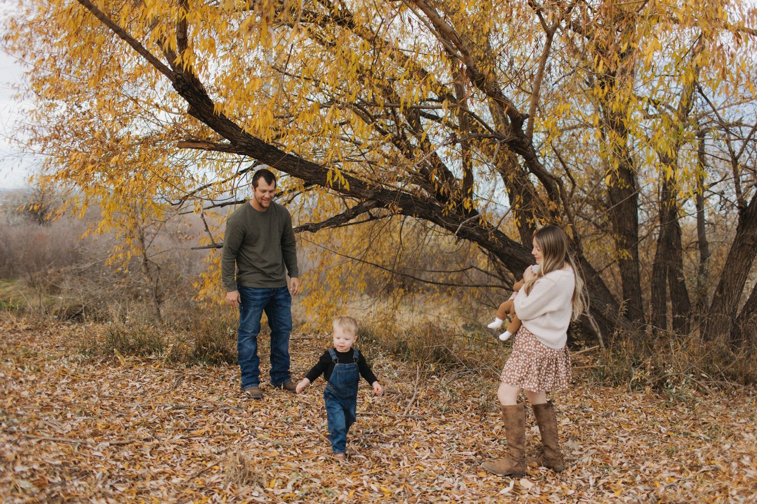 Family walking beneath golden autumn trees with fallen leaves.
