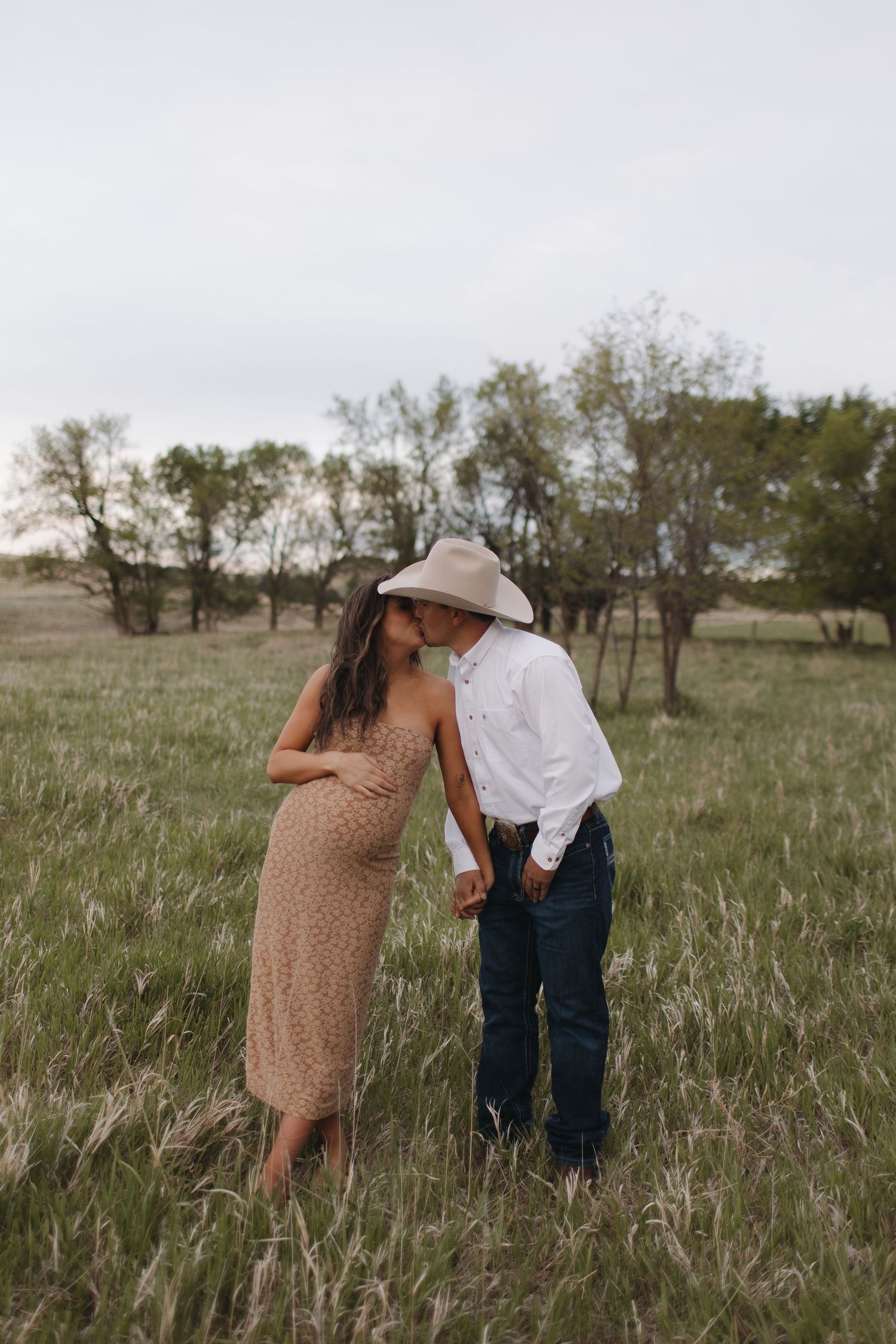 Couple sharing tender moments in a prairie field during golden hour.