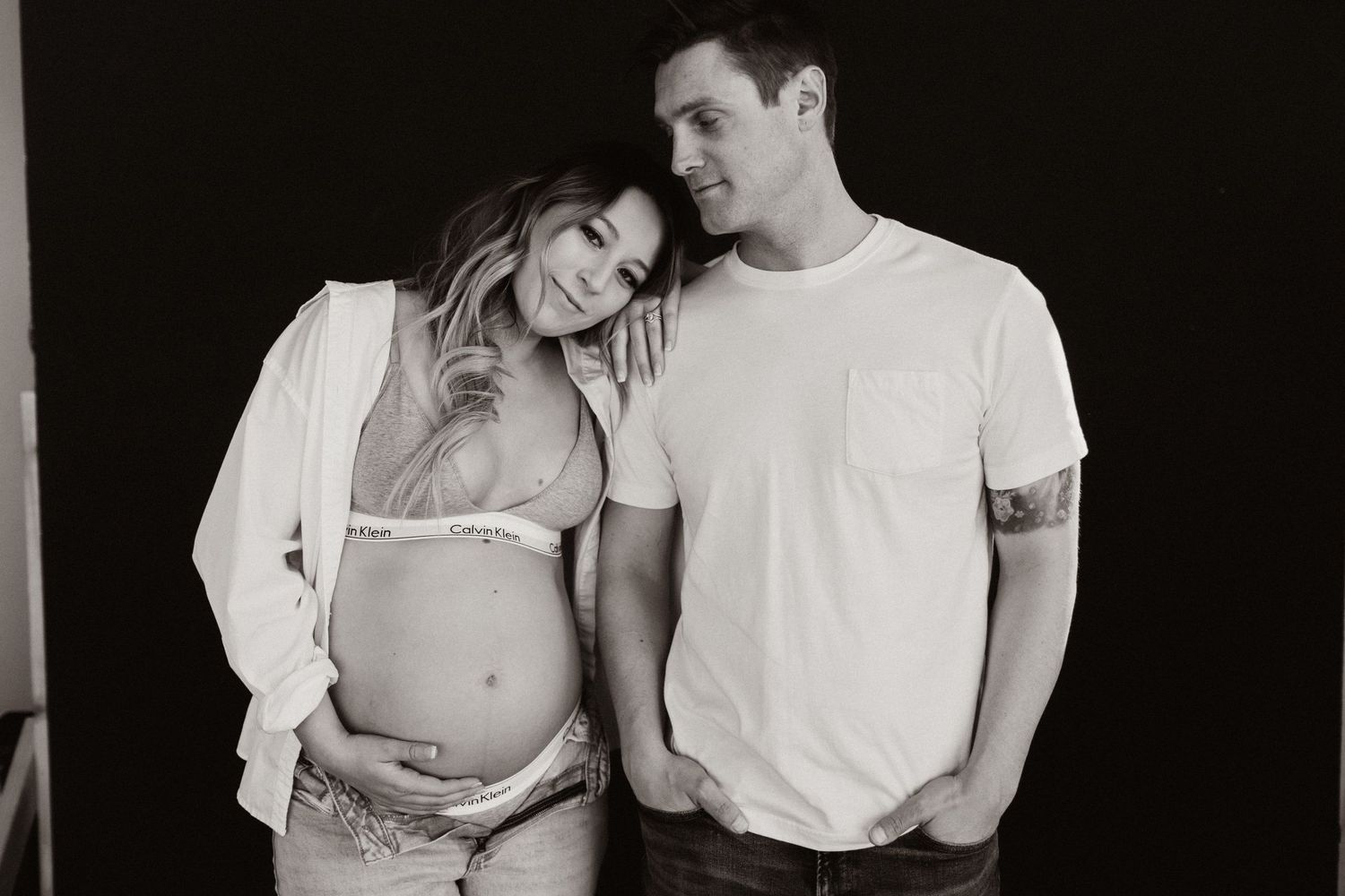 A black and white maternity portrait against a dark background.
