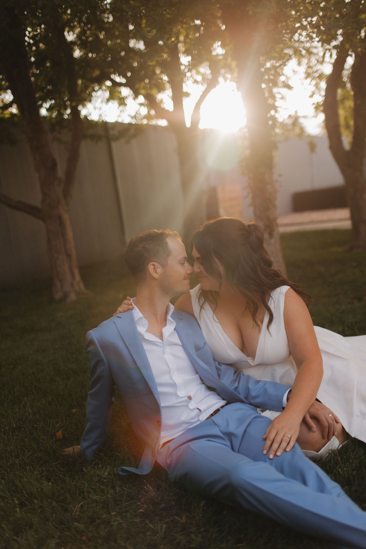 Couple in formal attire reclines on grass during golden hour sunset.