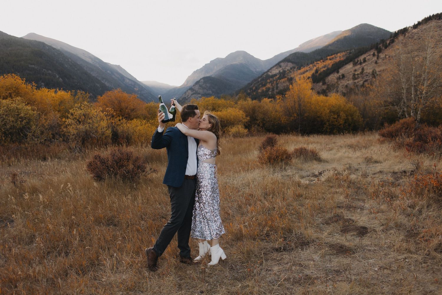 A couple shares a joyful moment in a mountain meadow surrounded by autumn colors.
