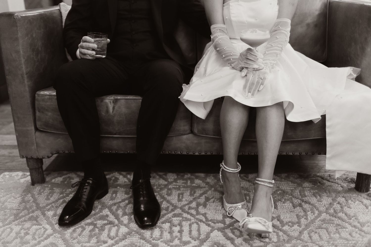Black and white photo showing feet and shoes of wedding party members lined up on patterned floor.