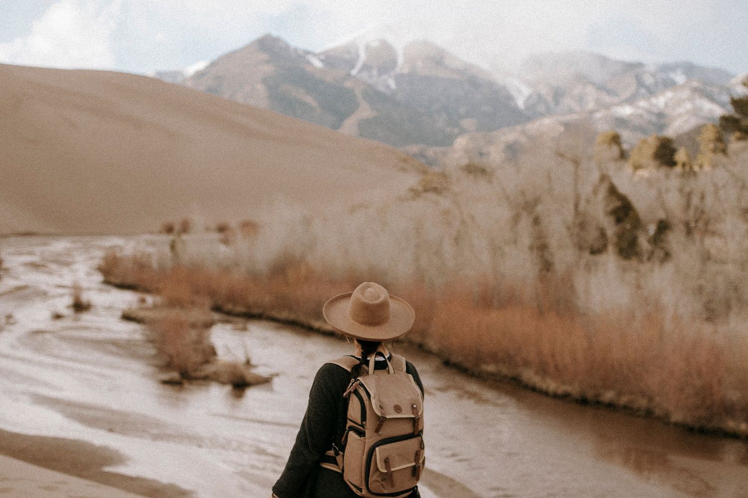 A hiker with backpack observes mountain scenery near a winding river in autumn.