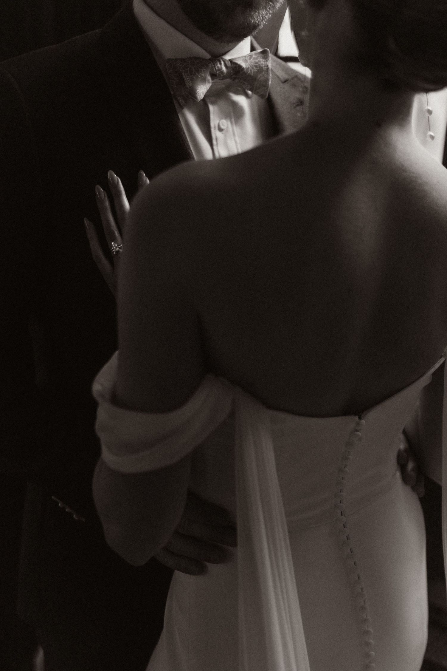 Dramatic black and white photos showing details of a wedding dress in low light.