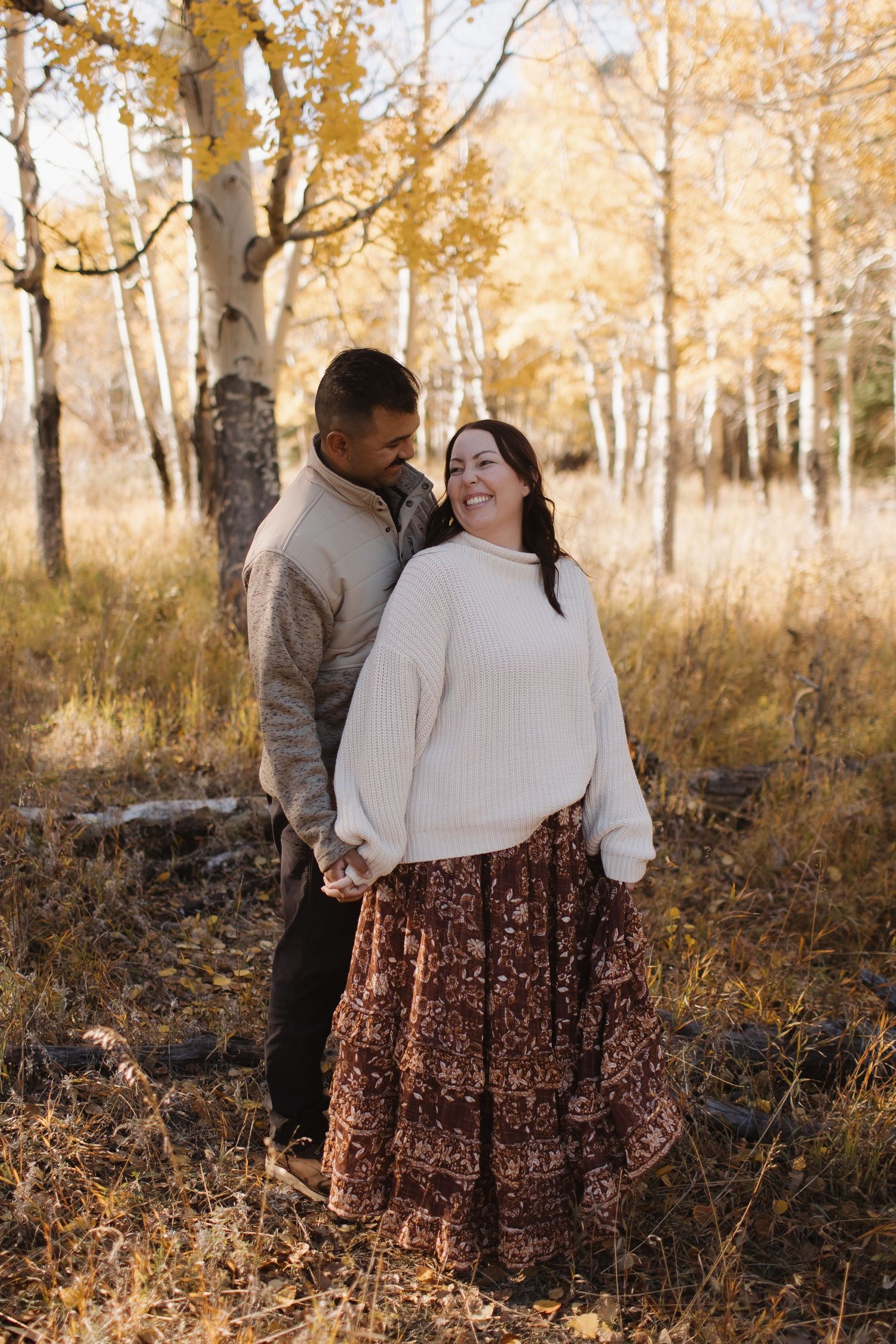 Couple embracing in autumn birch forest with golden sunlight filtering through trees.