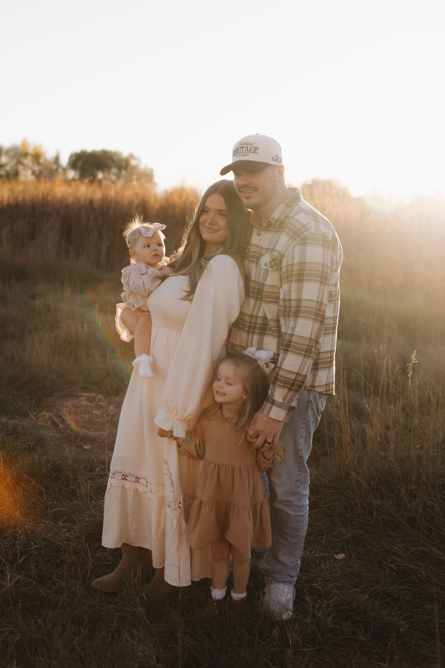 A family poses together in a field during golden hour with tall grass in the background.