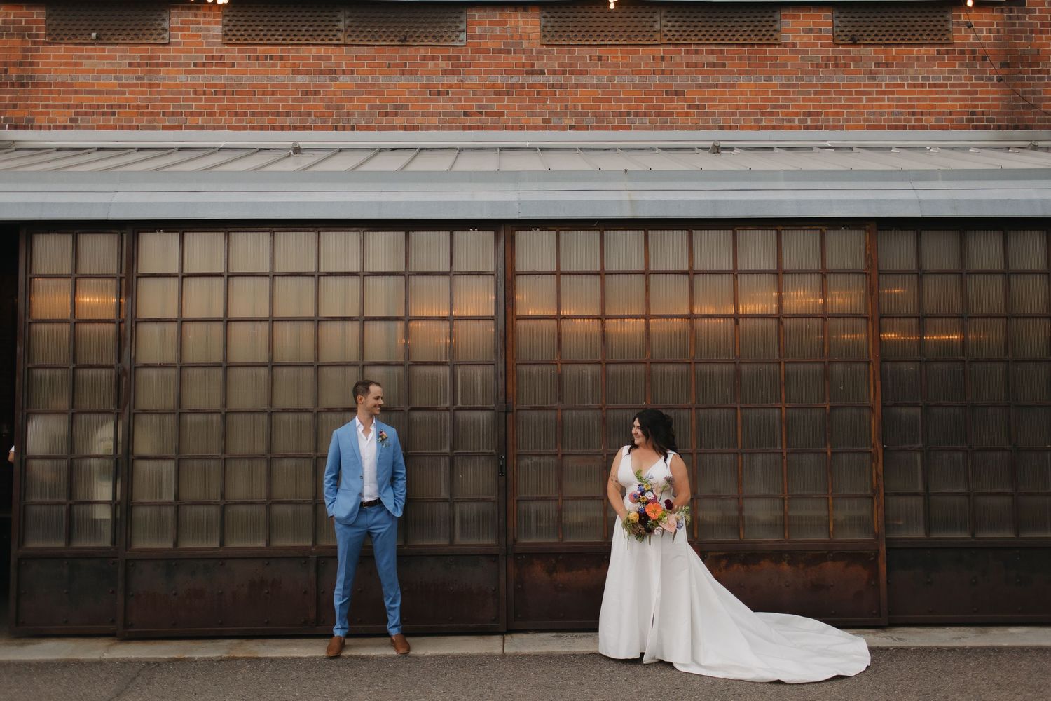 Wedding couple poses against industrial brick wall with garage doors for artistic portraits.