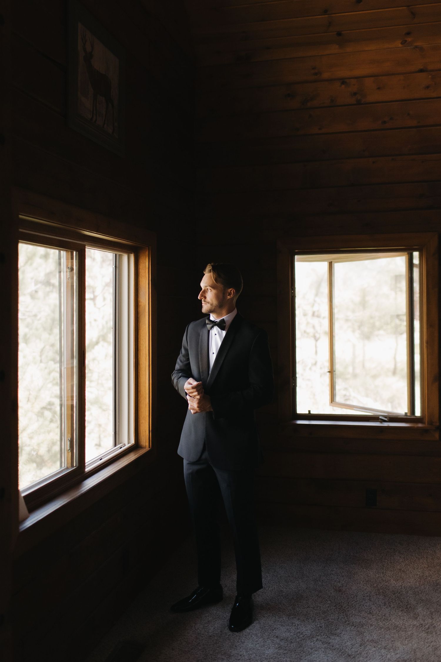 Silhouette of a person in formalwear standing by windows in a rustic wooden room.